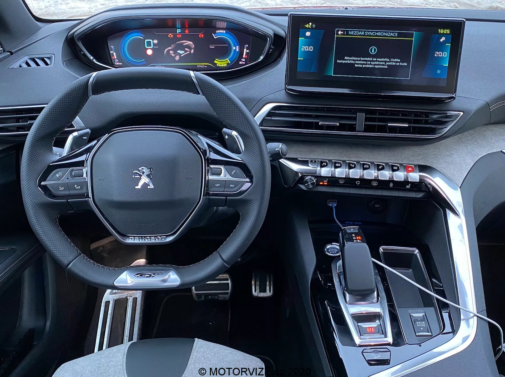 Pohled na interiér vozu Peugeot 3008 z roku 2021 z pohledu zadních sedadel, který ukazuje přední kabinu: moderní multifunkční volant s plochým spodkem a ovládacími tlačítky, digitální přístrojová deska, vyvýšená středová konzole s voličem rychlostí a elektronickou parkovací brzdou, samostatný dotykový infotainment systém, obdélníkové větrací otvory s ovladači klimatizace, elegantní interiér s materiálem připomínajícím kůži, kovovými akcenty, vysoce lesklou černou lištou, USB konektivitou, indikací automatické převodovky, držáky na nápoje a úložným prostorem.