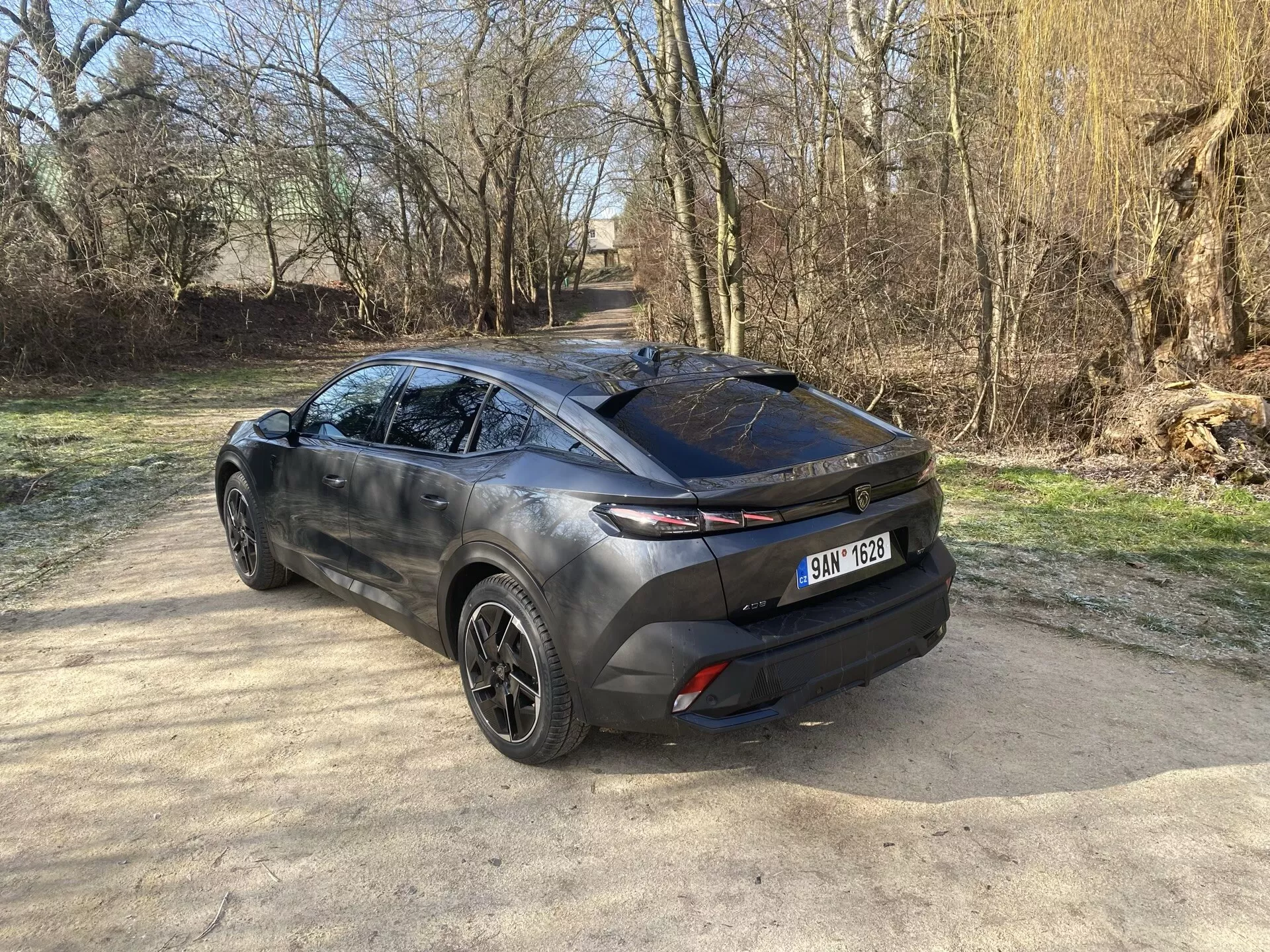 Zadní tříčtvrteční pohled na Peugeot 408 2023 ukazuje jeho moderní design crossoveru, zvýrazňuje záď, elegantní zadní okno a horizontální zadní světla protažená do boku karoserie, s náznakem slitinových kol, sochařského bočního profilu a dvoubarevného exteriéru na přirozeném slunečním světle