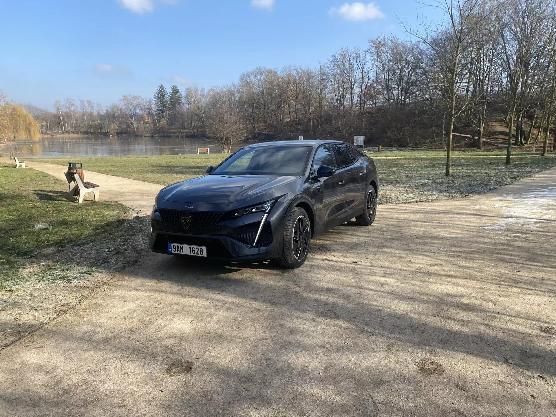 Peugeot 408 z roku 2023 zaparkovaný v přírodním prostředí během zimy nebo časného jara, prezentující jeho moderní crossoverový design, LED světlomety, přední senzorový systém, slitinová kola a prémiový finiš z pohledu z předního tříčtvrtečního úhlu pod slunečním světlem se zábleskem objektivu.