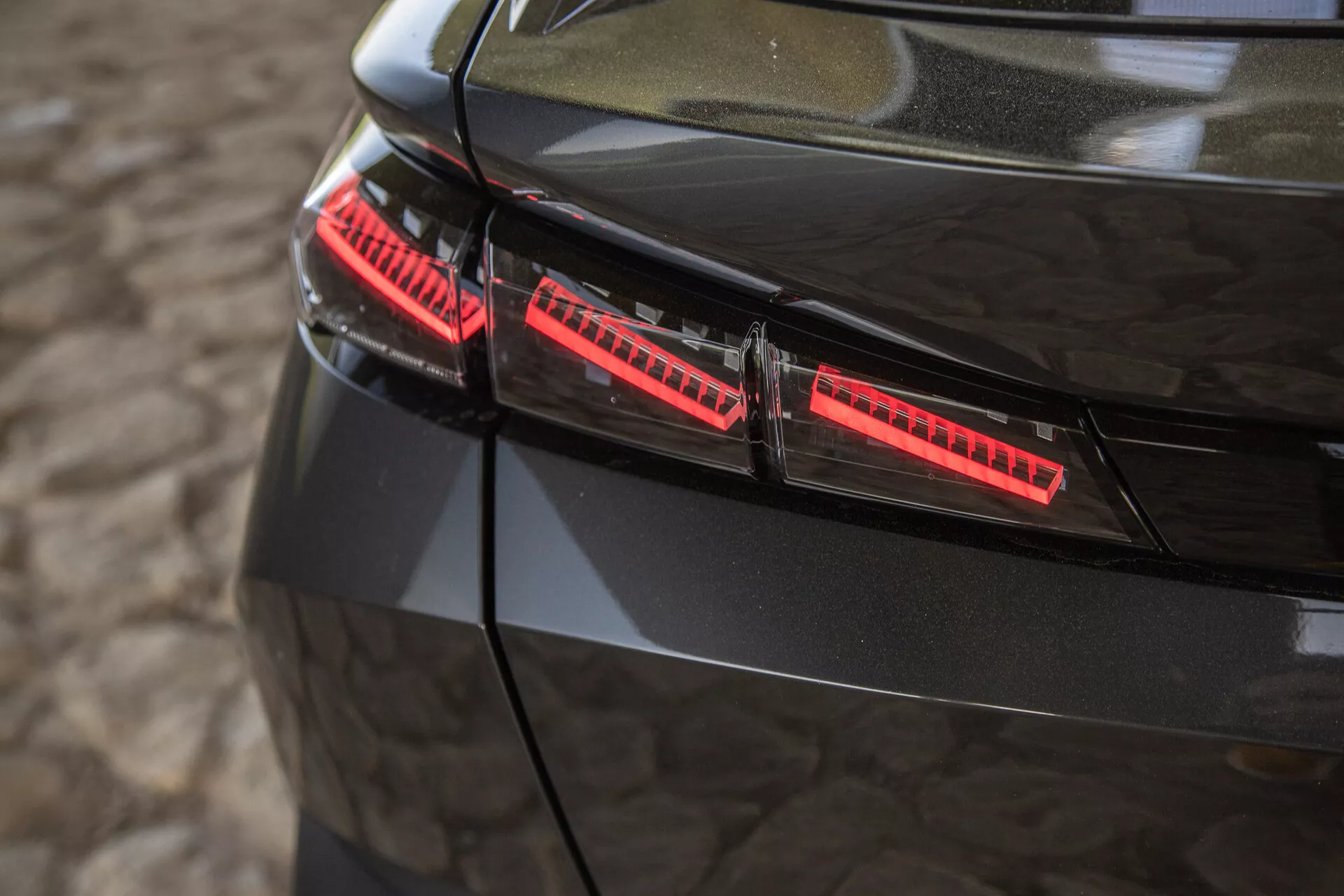 Detailní pohled na lesklé černé zadní světla Peugeotu 408 z roku 2023 s moderními LED prvky a elegantními designovými akcenty zachycenými z mírně zvýšeného úhlu