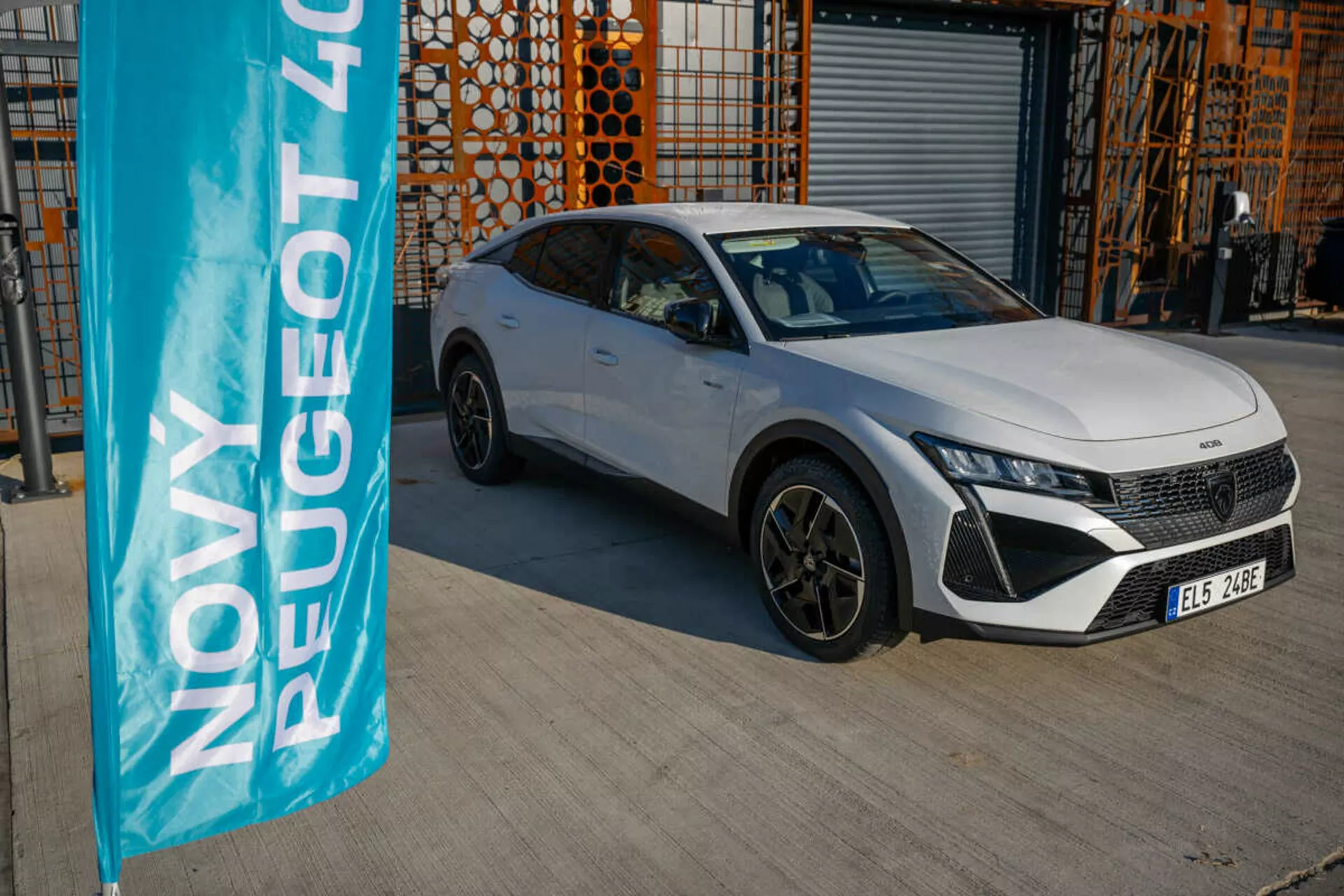Bílý Peugeot 408 ročník 2023 zaparkovaný venku s průmyslovou architekturou na pozadí, předvádějící designové a technologické funkce vozidla pod přirozeným denním světlem