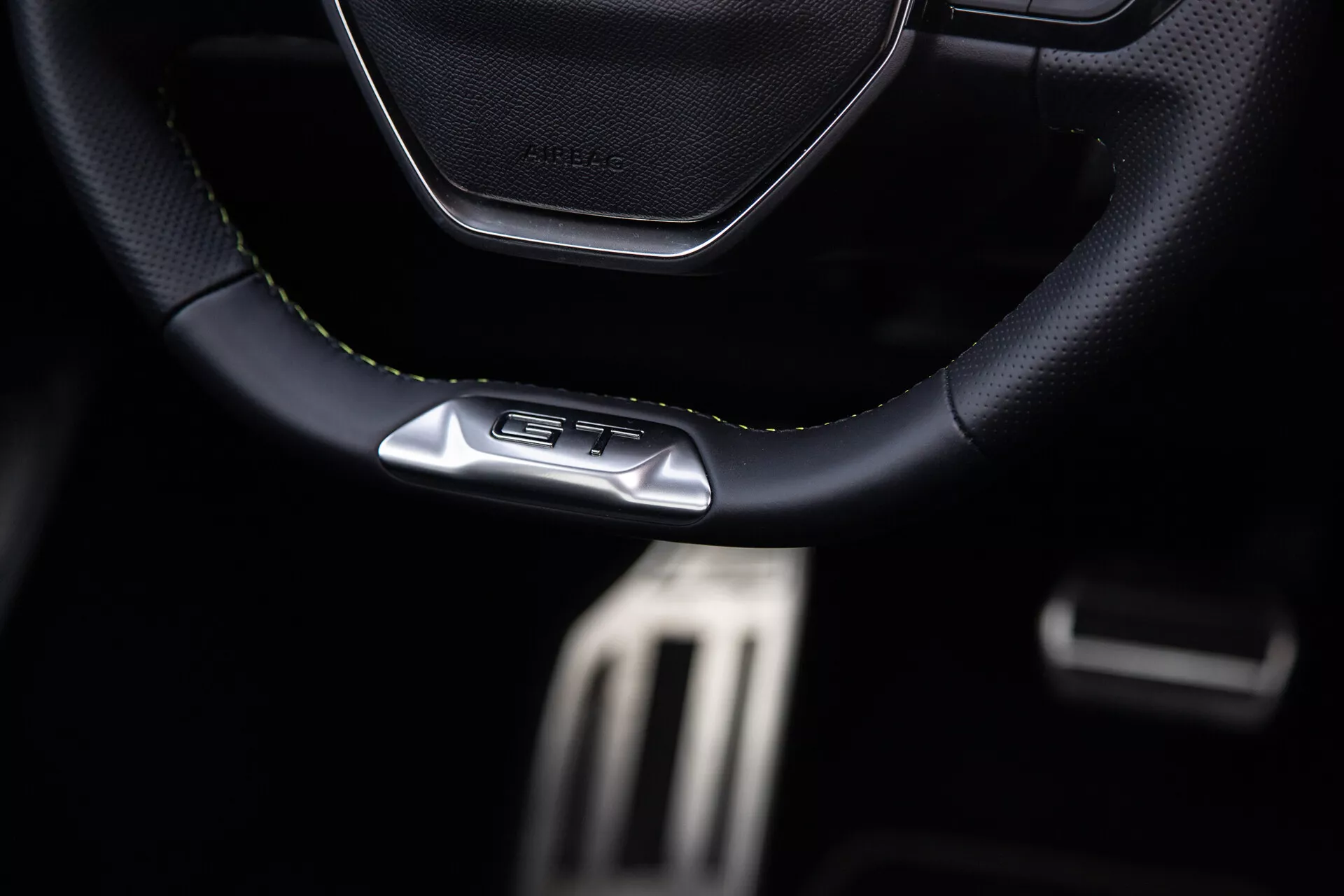 Interiér Peugeotu 408 pro rok 2023 se zaměřením na sportovní volant se stehy z kůže či materiálu podobného kůži s emblémem GT, kovové pedály pro výkon a prvky prémiového tmavého kokpitu