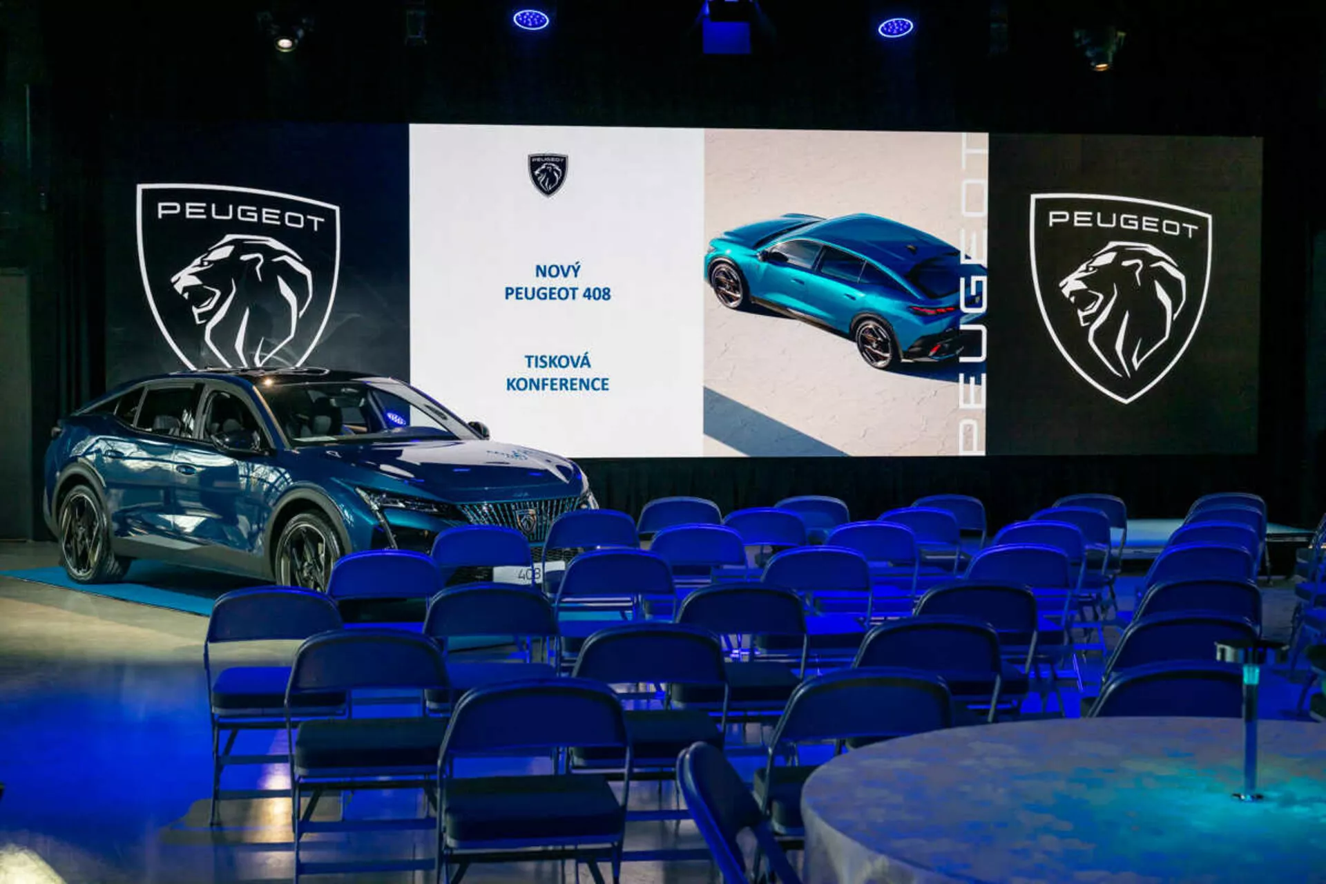 Peugeot 408 prezentovaný na tiskové konferenci, zobrazen pod úhlem 45 stupňů, který zdůrazňuje jeho přední a boční profily, elegantní design a LED světlomety, s digitálními obrazovkami a brandingem na pozadí