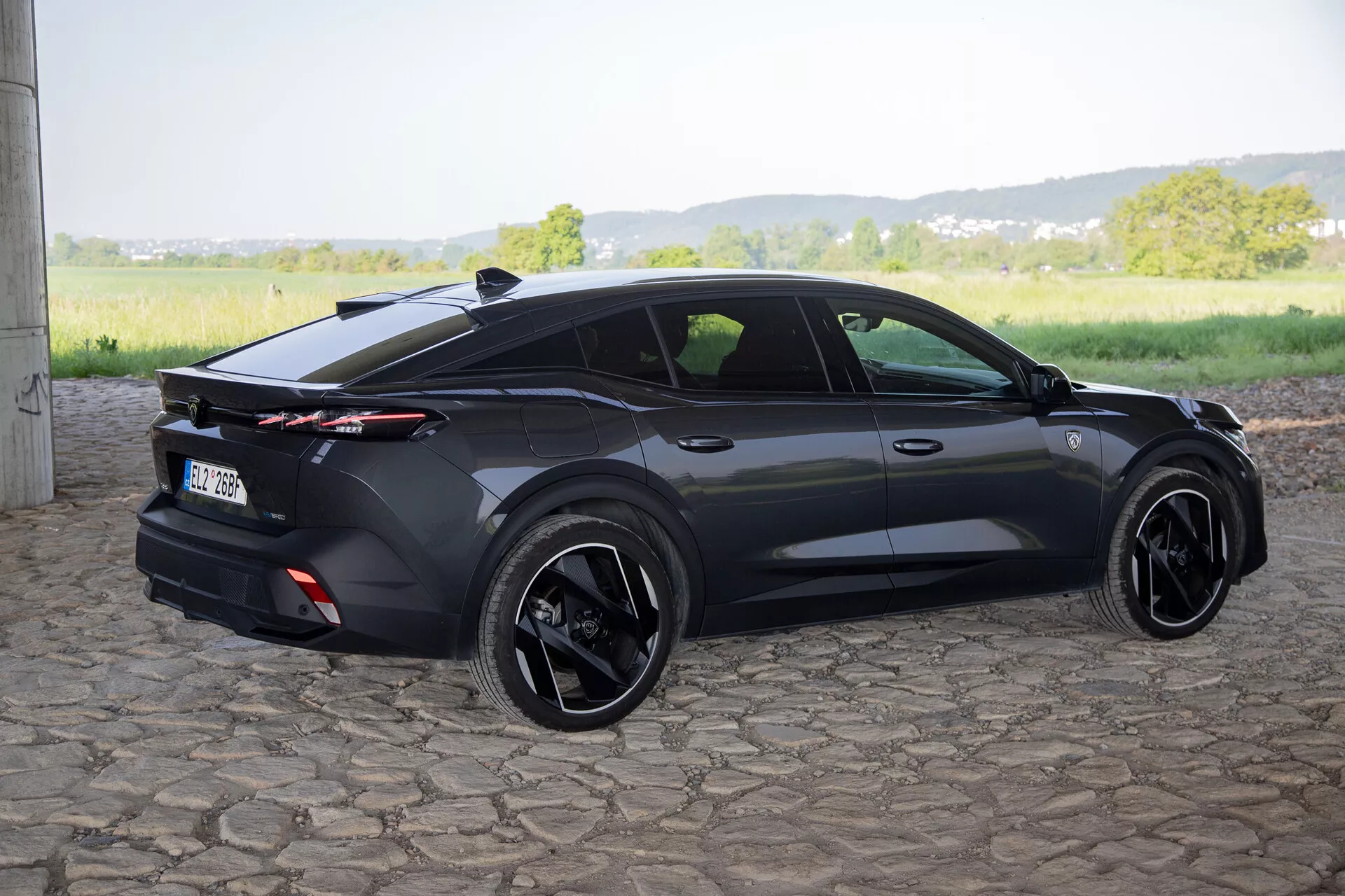 Peugeot 408 z roku 2023 zachycený z úhlu tři čtvrtě zezadu, který zdůrazňuje jeho sportovně elegantní design hatchbacku, integrované zadní spoiler s celoplošnými zadními světly, černé slitinové kola a současné prvky jako jsou zapuštěné kličky dveří a boční zrcátka s blinkry, na přirozeném denním světle