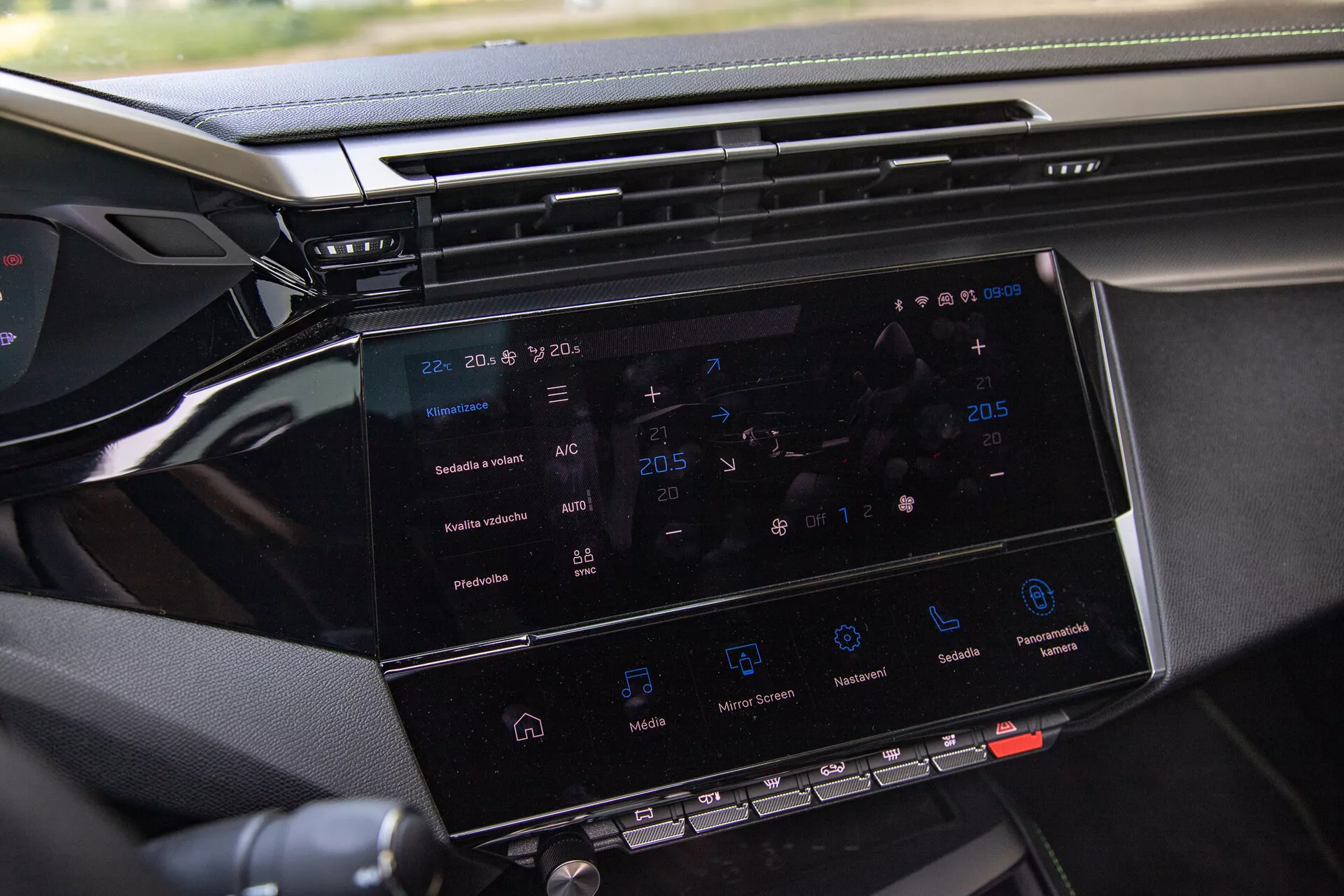 Detailní záběr infotainment systému Peugeot 408 2023 ukazující 8-10 palcový dotykový displej s navigací, ovládáním klimatizace, ikonami pro přehrávání médií a náhledem na palubní desku, pořízeno z místa spolujezdce