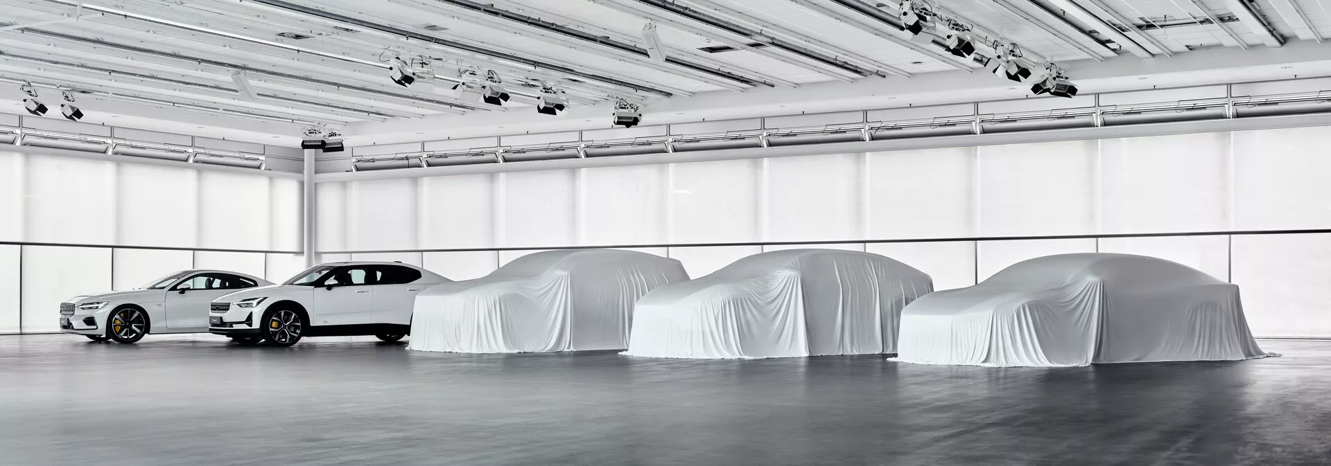 Debut Polestaru 3 roku 2023, prezentace moderního sedanu s aerodynamickým designem ve vnitřním výstavním prostoru, obklopen siluetami budoucích modelů pokrytých plachtami