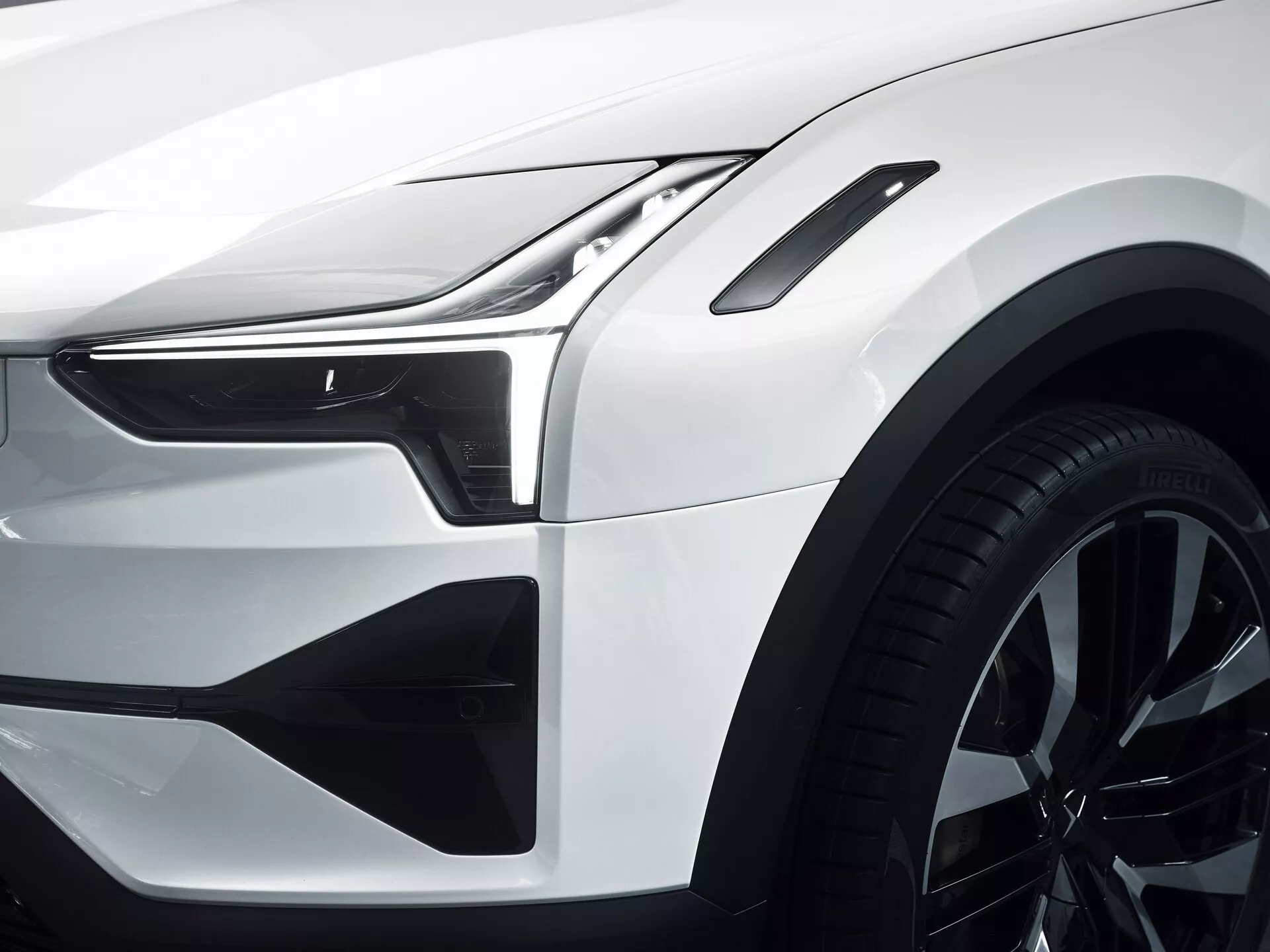 Detailní pohled na přední čtvrtinu Polestar 3 2023 s LED světlometem a denními světly, aerodynamickými konturami kapoty a blatníku, stylovými vzduchovými vstupy na předním nárazníku, slitinovým kolem s více paprsky, přesnými mezerami panelů a čistými liniemi karoserie, lesklým bílým provedením, což naznačuje pokročilý design a technologii automobilů
