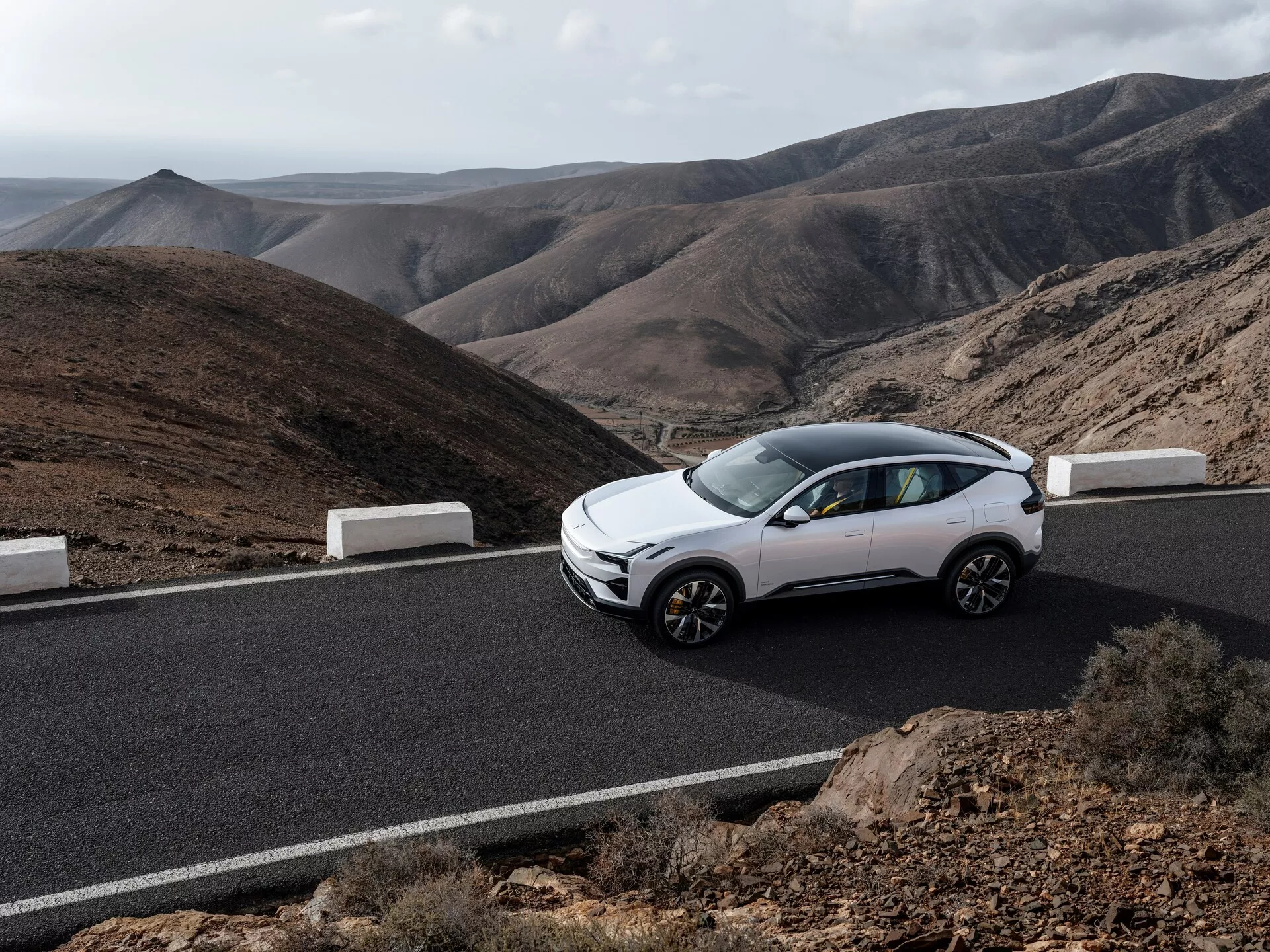 Polestar 3 první generace 2023, bílá barva, pohled z čelního bočního úhlu na asfaltové silnici s horami na pozadí, zdůraznění moderního designu crossoveru, kompaktních funkcí SUV a slitinových kol pod přirozeným světlem.