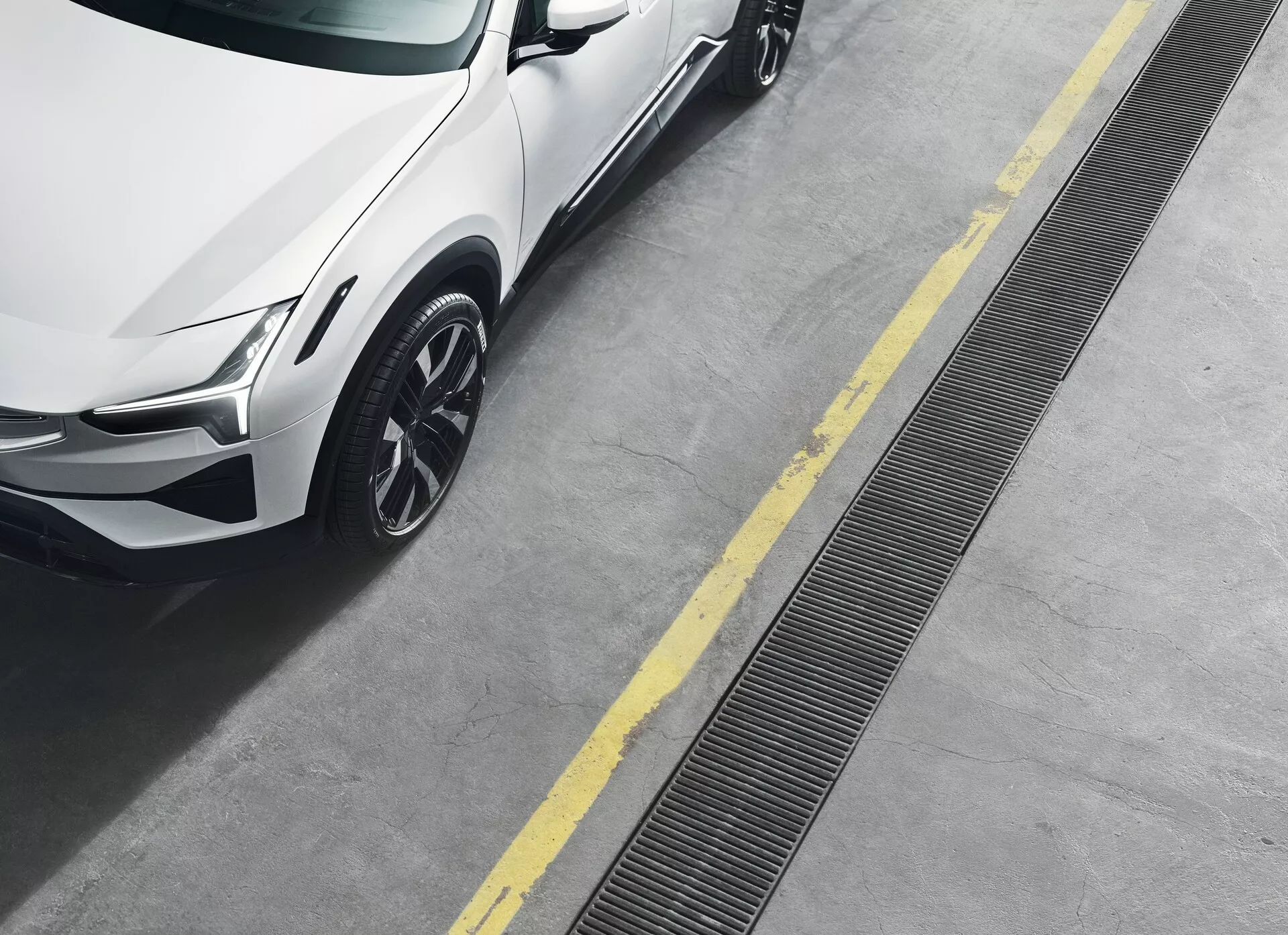 Polestar 3 z roku 2023, 1. generace, zobrazen z vysokého úhlu s důrazem na přední pravou část včetně LED světlomety, metalického laku, lité kola s vícepaprskovým designem a dynamických linií karoserie na čistém betonovém povrchu s žlutými parkovacími čarami.