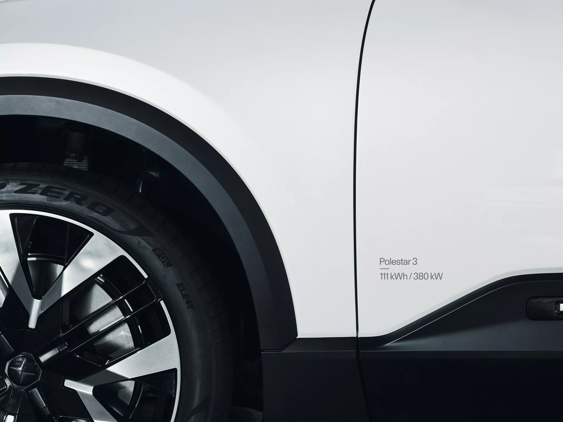 Detailní pohled na Polestar 3 2023 zobrazující přední kolo s pneumatikou Pirelli P Zero a boční panel, představující design slitinového kola s mnoha paprsky a odznak s údaji o výkonu 11kW/380kW, což zdůrazňuje jeho elektrické výkonnostní schopnosti a elegantní bílý design.
