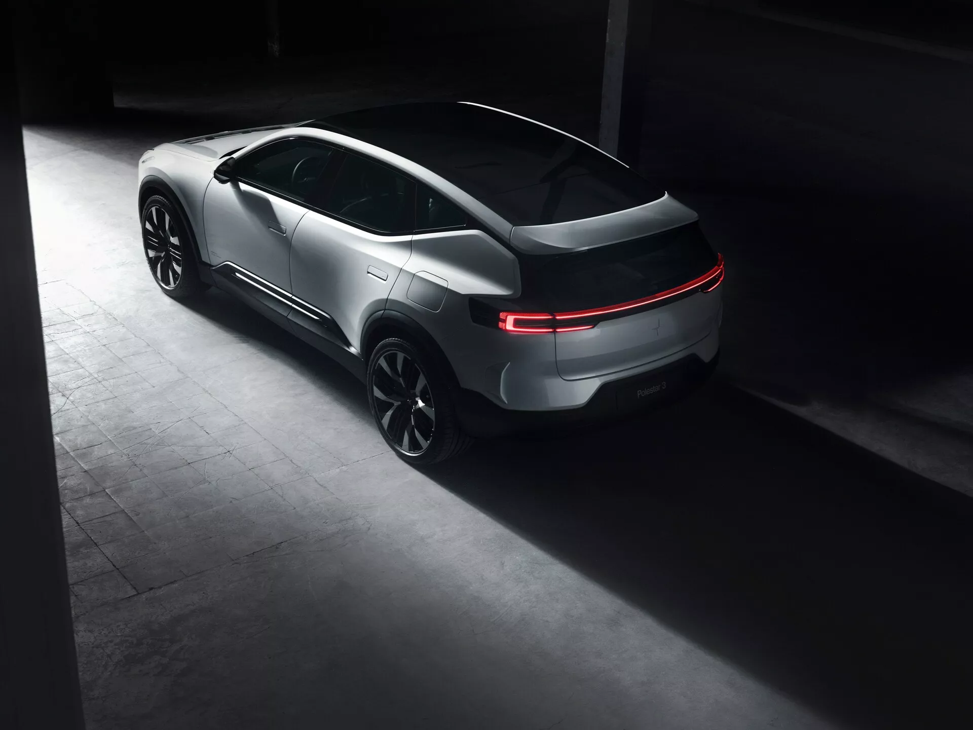 Polestar 3 první generace roku 2023, prezentující elegantní design ve stylu kupé s osvětlenými zadními LED světly a sportovními velkými slitinovými koly v šerém, luxusním prostředí zdůrazňujícím jeho luxusní a moderní vzhled