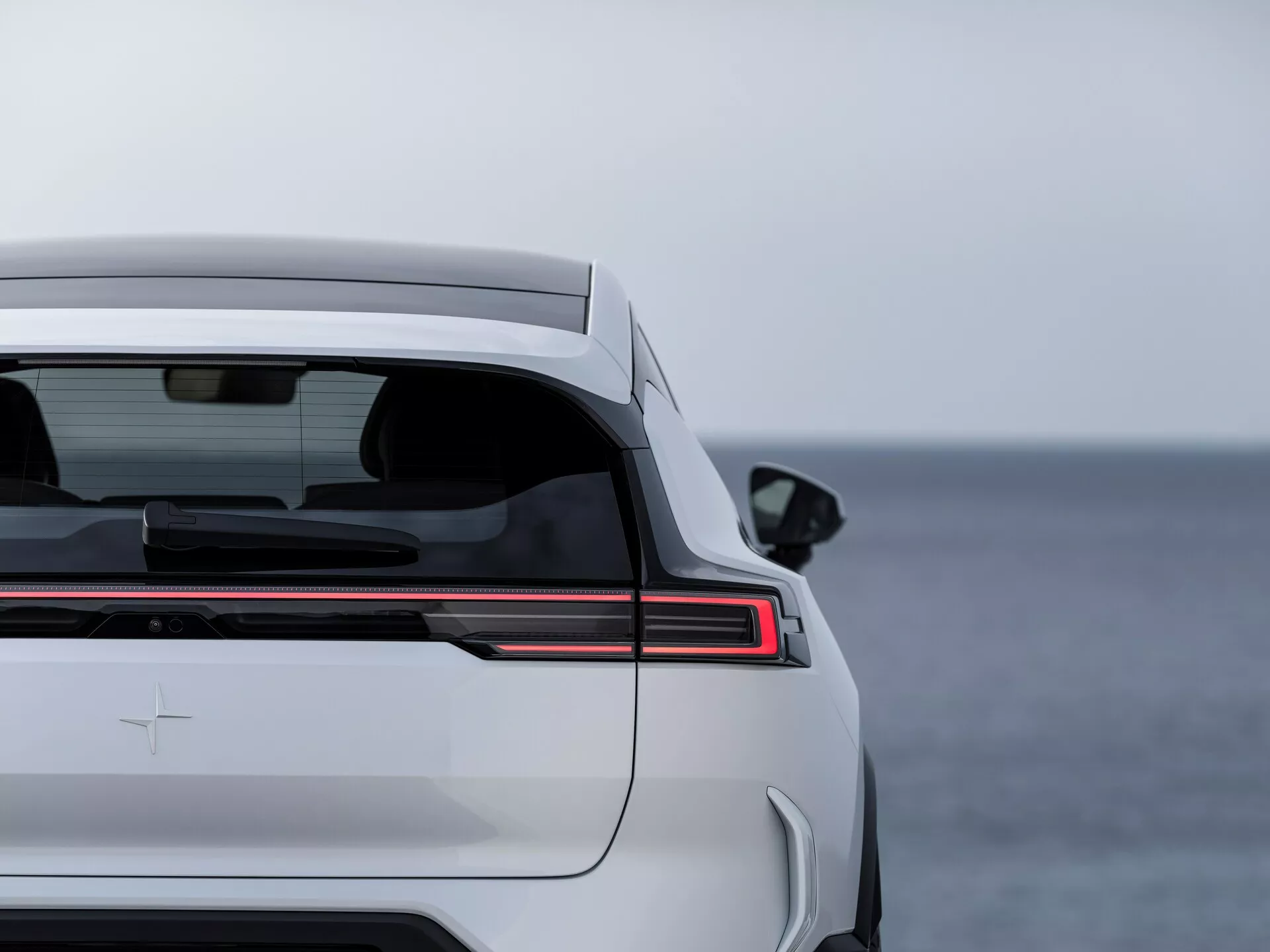 Polestar 3 první generace roku 2023 prezentující zadní designové prvky, včetně horizontálního LED pruhu zadního světla, zatmaveného zadního okna s odmlžovačem, integrovaného spoileru kufru a prémiového znaku na pozadí s otevřenou vodou.