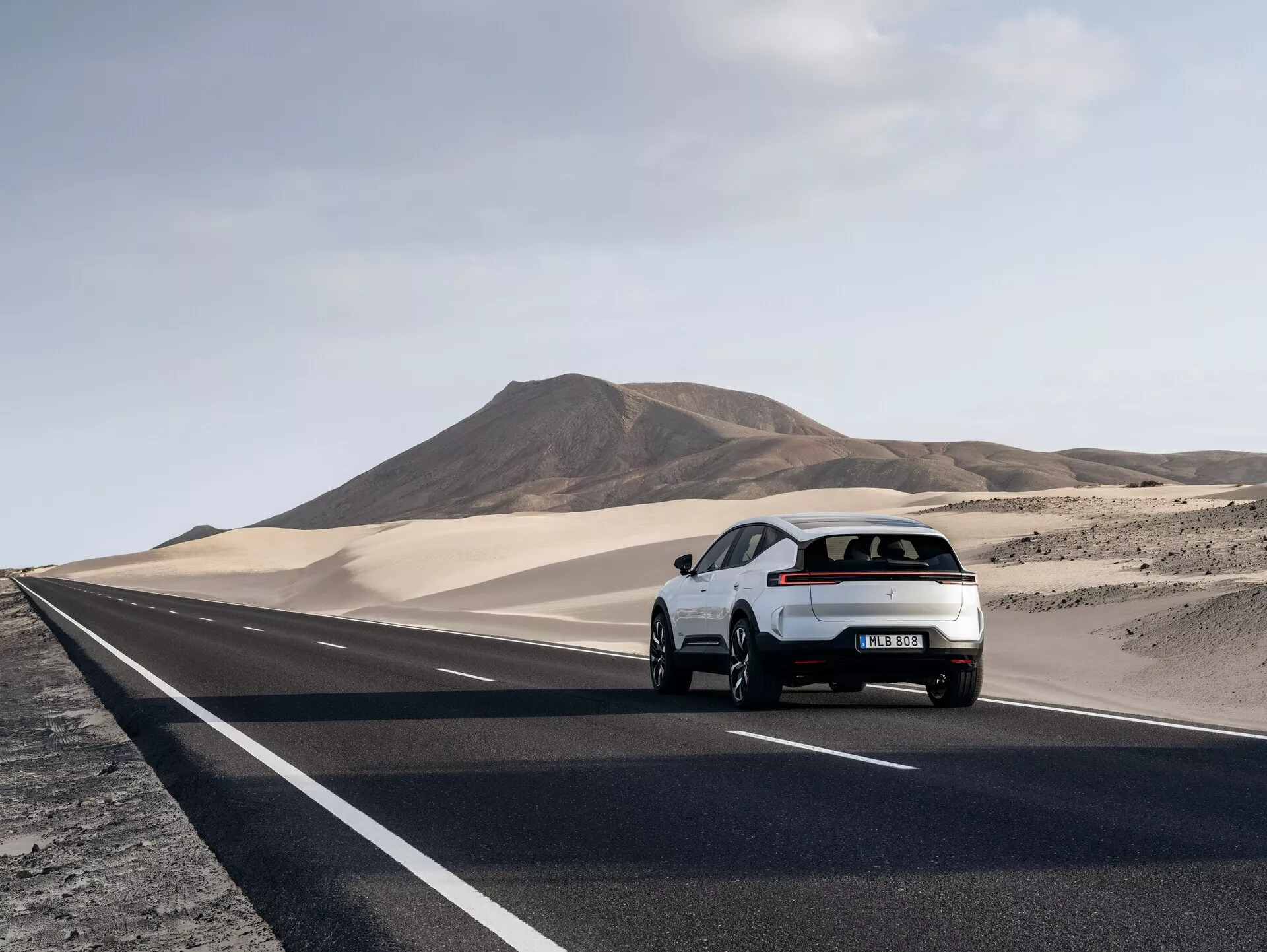 Hatchback Polestar 3 roku 2023 jedoucí po pouštní silnici, zobrazující jeho zadní levou stranu a aerodynamický design s LED zadními svítilnami