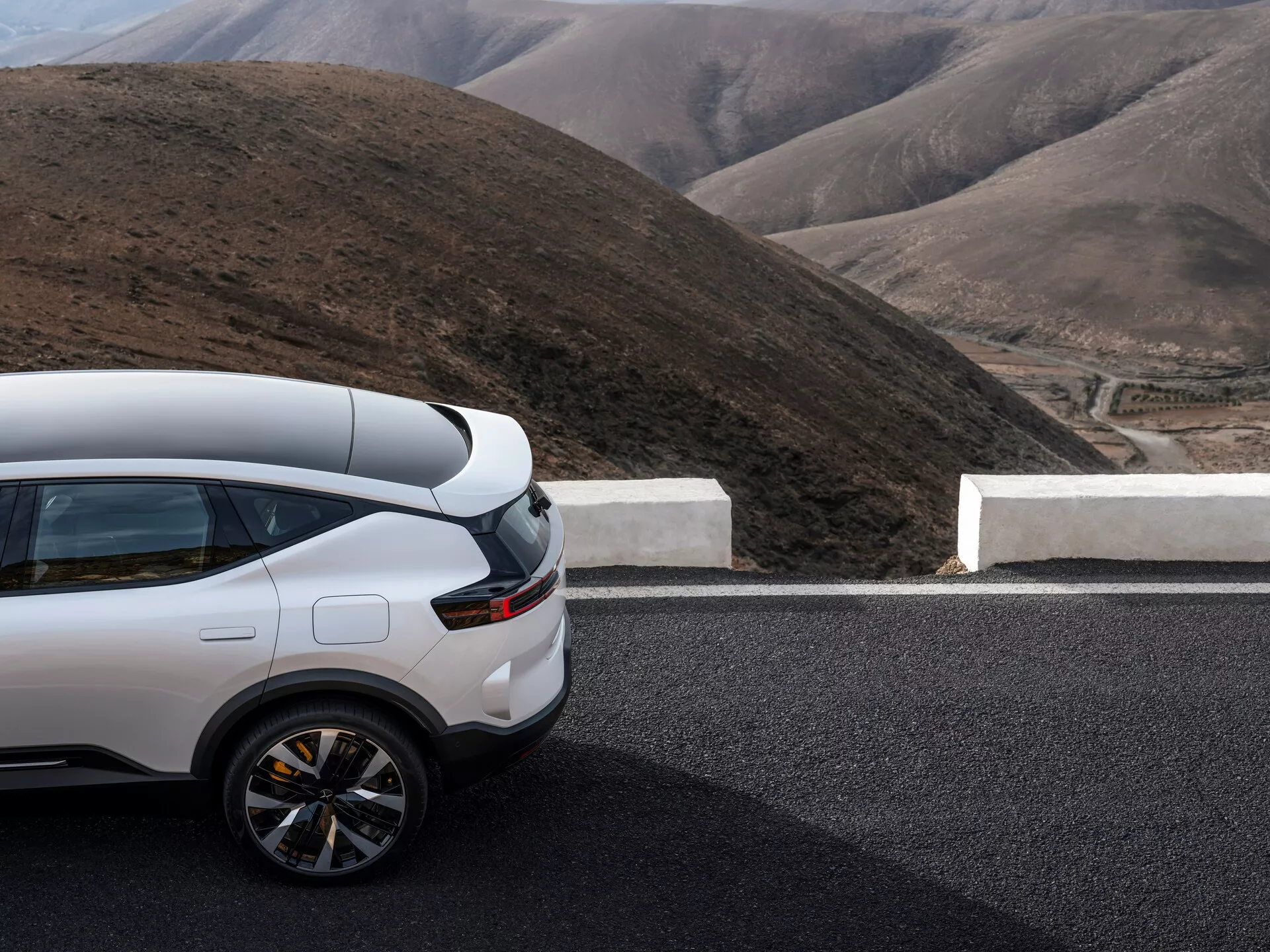 Polestar 3 první generace roku 2023 s částečným pohledem na bok a zadní část na silnici, s high-tech bílým SUV na pozadí horské krajiny zdůrazňujícím sportovní zadní část, současný design zadních světel a luxusní boční profil