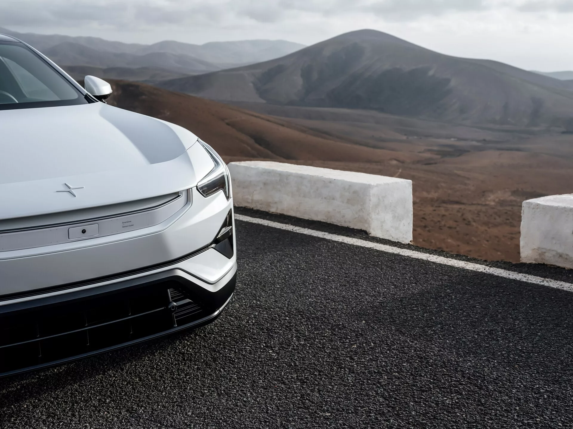 Detailní pohled na přední část sedanu Polestar 3 z roku 2023 s pokročilou aerodynamikou, designem elektrického vozidla s LED světlomety a pozadím horské krajiny