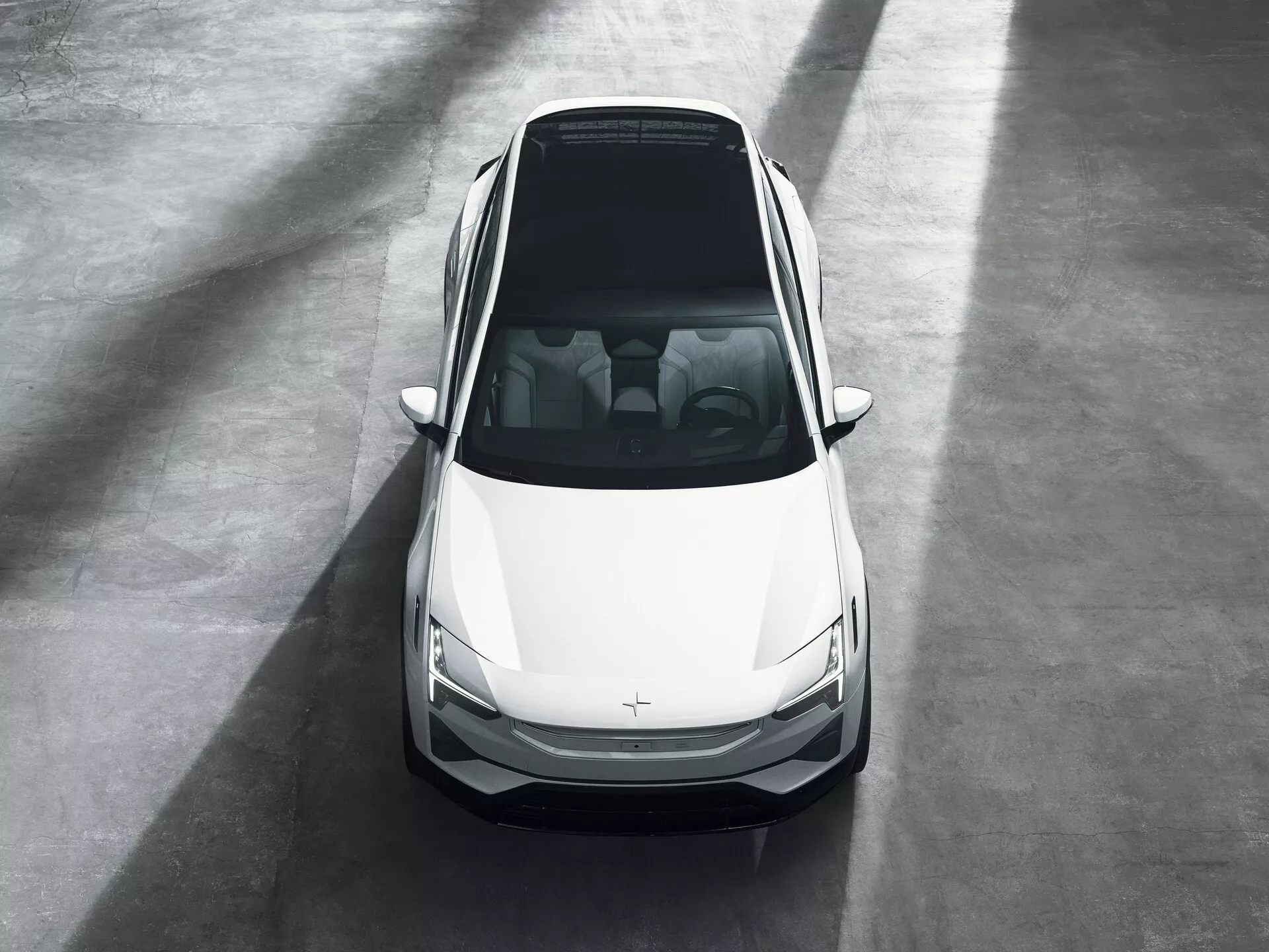 Sedan první generace Polestar 3 2023 zobrazený z vysokého čelního úhlu v prostředí showroomu, zdůrazňující jeho moderní design, bílou barvu a prvky na přední straně včetně kapoty, střechy, čelního skla, předních dveří, štíhlých LED světlometů a mřížky s nezřetelným znakem, naznačující možné atributy elektrického vozidla