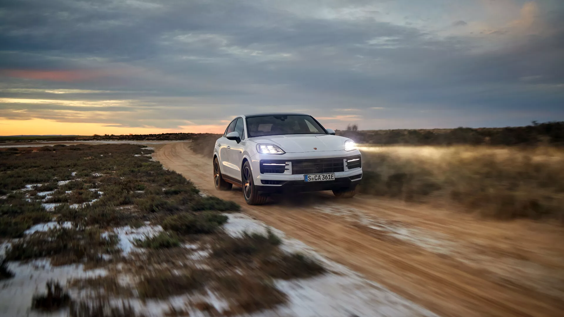 Model Porsche Cayenne 9YA Facelift 2023 jedoucí v terénu, ukazující jeho tříčtvrteční přední pohled s LED světlomety, aktivním zavěšením a systémem pohonu všech kol v soumrakovém nastavení