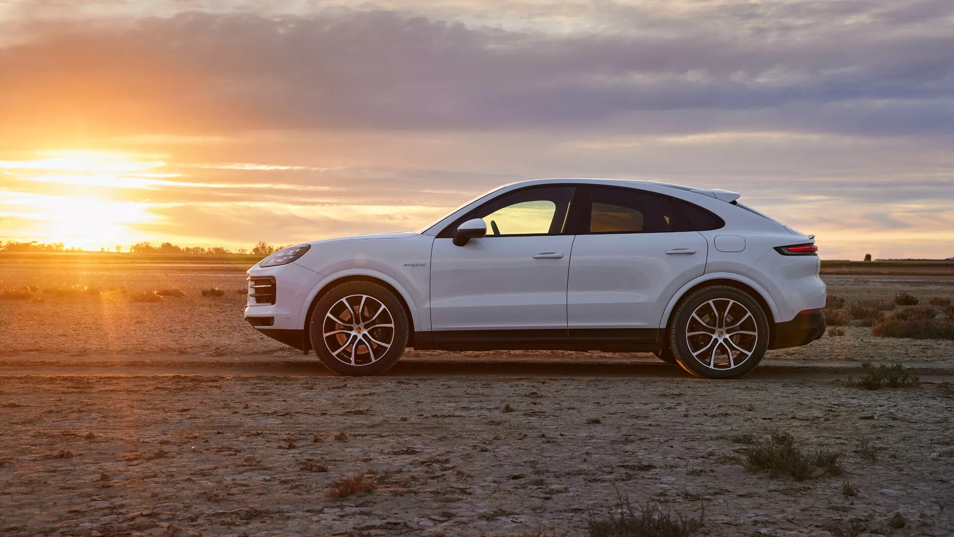 Luxusní crossover SUV Porsche Cayenne 2023 v lesklé bílé barvě na aridním terénu ve zlaté hodině, zobrazující profilový pohled, sportovní slitinová kola a elegantní designové prvky