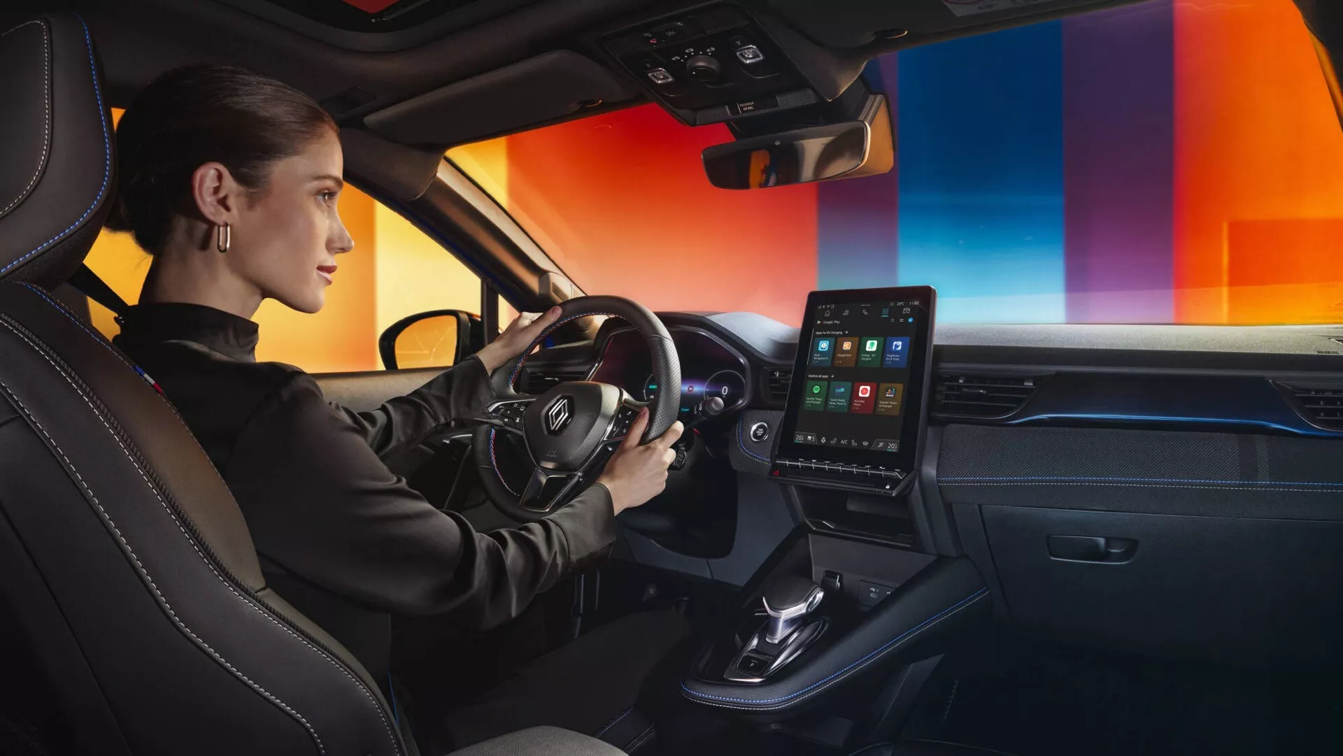 Vnitřní pohled na Renault Captur II-Facelift 2024 se zaměřením na stranu řidiče z pravého středního úhlu, ukazující volant s multifunkčními tlačítky, digitální přístrojový panel, orientovaný k řidiči dotykový displej infotainmentu, minimalistickou konzolu, venty automatické klimatizace, páku automatické převodovky, prvotřídní materiálové provedení, sportovní sedadla s koženým čalouněním a kontrastním prošíváním a ambientní osvětlení palubní desky.