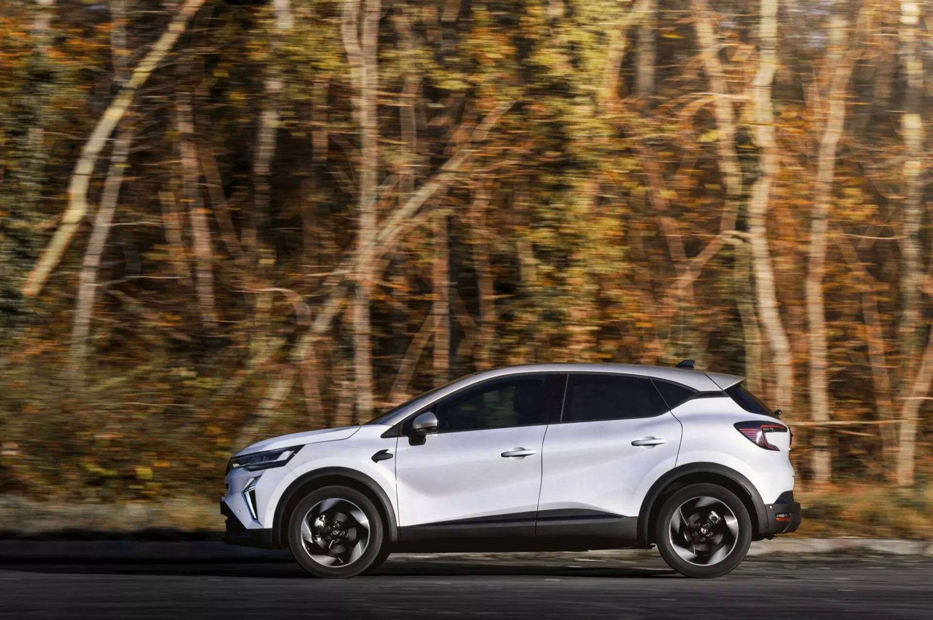 Renault Captur 2024 (II facelift) jedoucí po lesní cestě, zobrazuje celý boční profil s elegantním designem, výraznými koly a náznakem zadních designových prvků