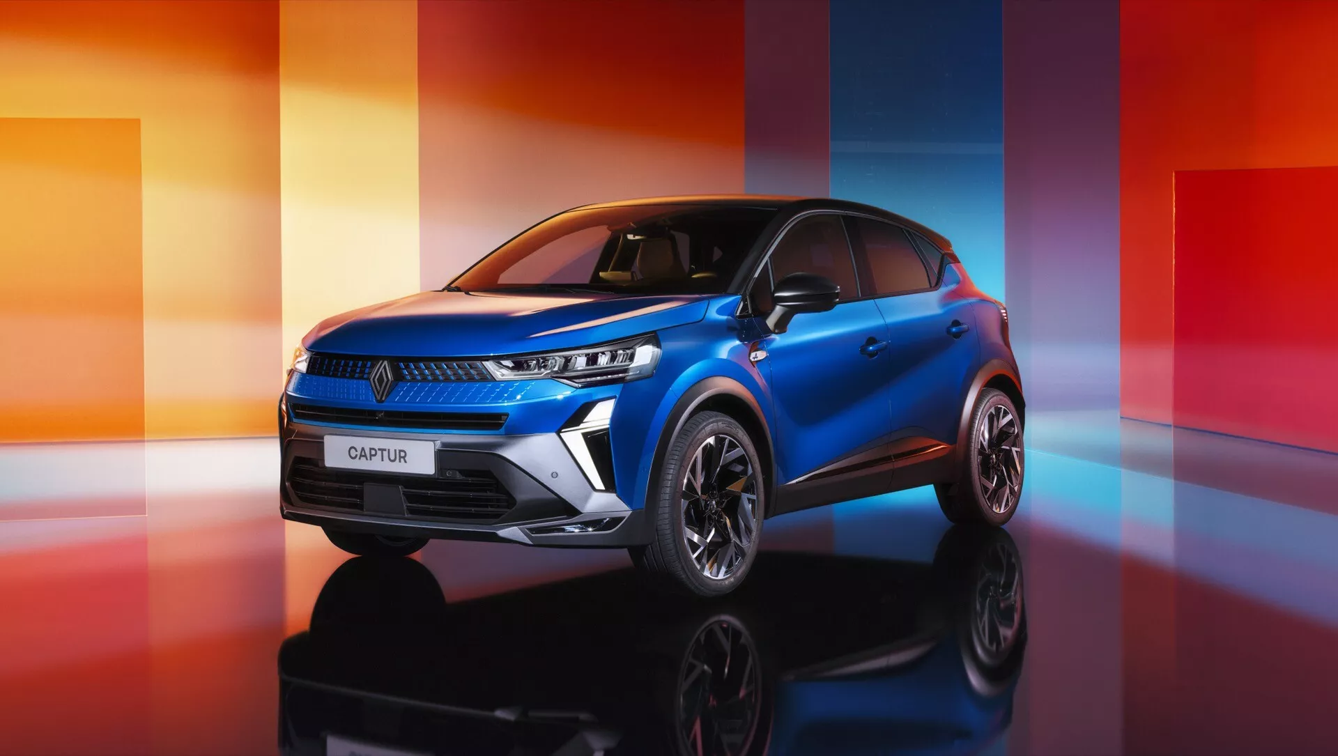Facelift Renault Captur II 2024 zachycen z pohledu tří čtvrtin zepředu, předvádějící jeho elegantní LED světlomety, stylová slitinová kola a vysoce kvalitní modrou barvu v prostředí studia
