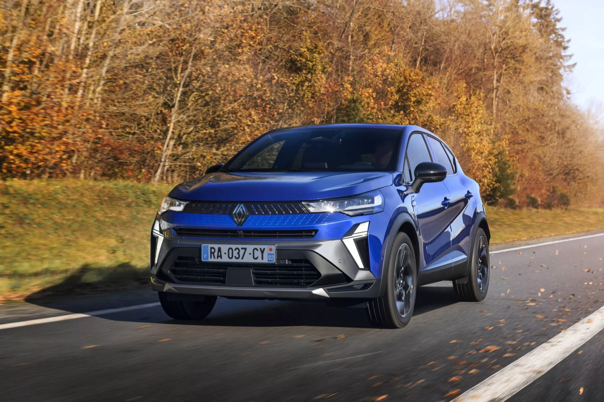 Renault Captur 2024 po faceliftu v pohybu, zobrazuje moderní modré SUV s úzkými úhlovými světlomety a výraznou maskou na dálnici, zdůrazňuje sportovně elegantní vzhled, slitinová kola a dynamické designové prvky ve dne.