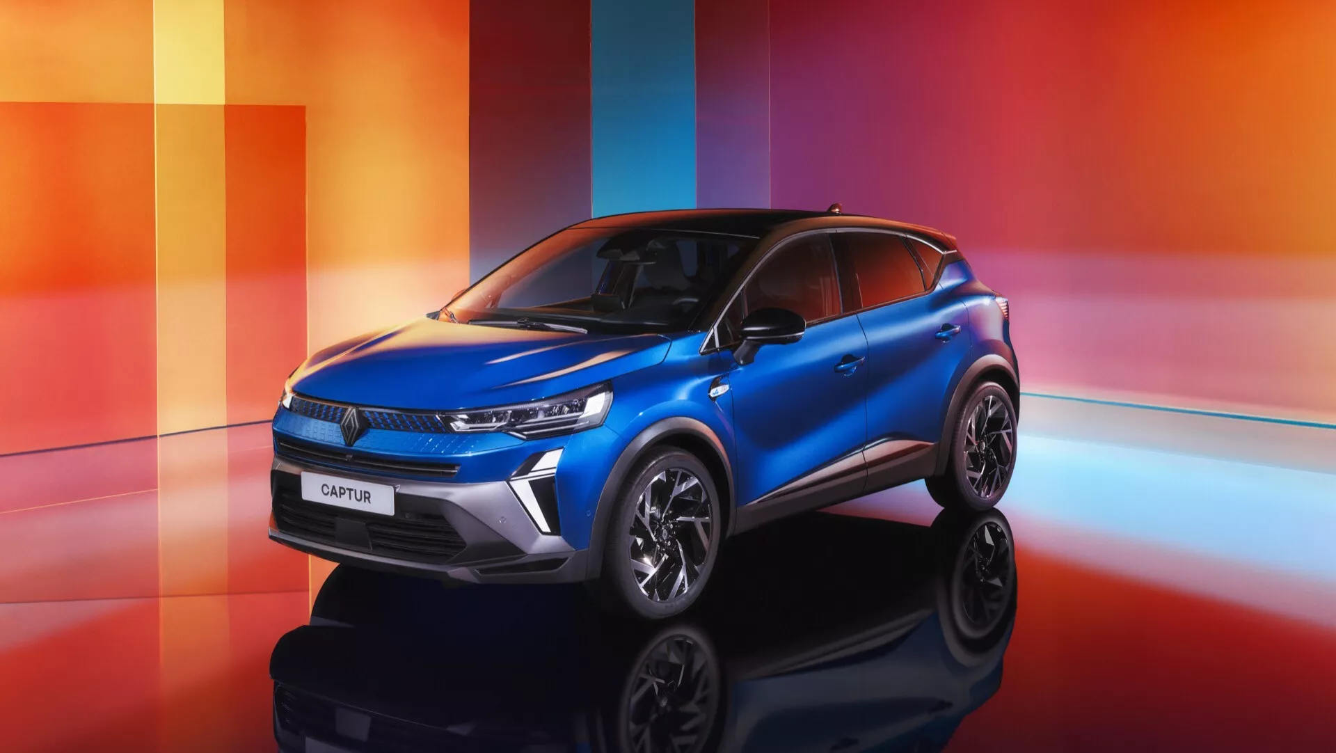 Renault Captur 2024 (II Facelift) prezentován na barevném geometrickém pozadí s odstíny oranžové, červené a fialové, zdůrazňující jeho moderní SUV design, úzká LED světla, vodorovná mřížka s emblémem značky, tvarovaná kapota pro zvýšenou aerodynamiku, sportovní kola z lehkých slitin a stylový dvoubarevný lak.