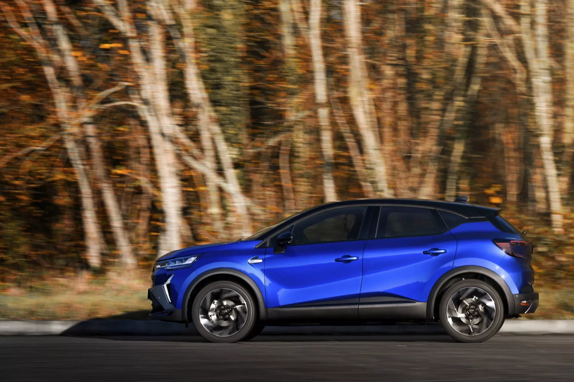 Renault Captur (II-Facelift) 2024 v pohybu, modré SUV s dynamickou technikou panning zdůrazňující rychlost a detaily designu, boční profilový pohled na scénické silnici
