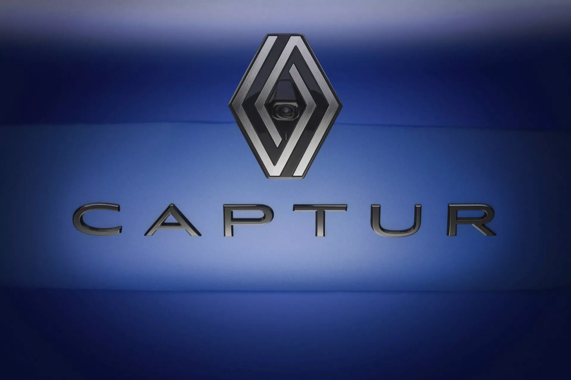 Emblém modelu Renault Captur II-Facelift 2024, se znakem ve tvaru chromovaného diamantu na černém pozadí a nápisem CAPTUR na pozadí modrého gradientu