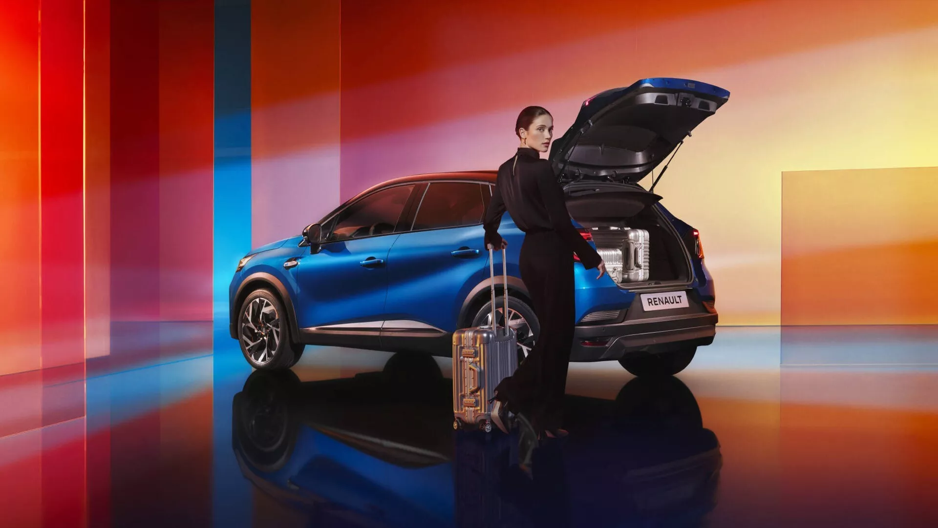 Facelift Renault Captur II 2024 v jasně modré barvě, boční a částečný zadní pohled s otevřeným elektrickým zavazadlovým prostorem a velkými koly, na pozadí s dynamickým přechodem z červené do oranžové