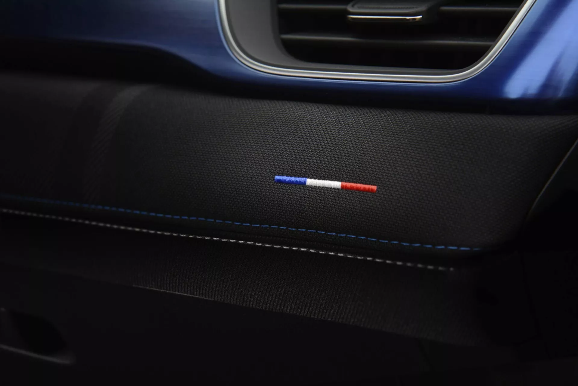 Detailní snímek interiérového bočního panelu Renault Captur 2024 s jemným prošíváním na prémiové černé kůži, dvoubarevné ambientní osvětlení v červené a modré a elegantní černé a modré lemování, představující elegantní designové prvky a pokročilou technologii osvětlení