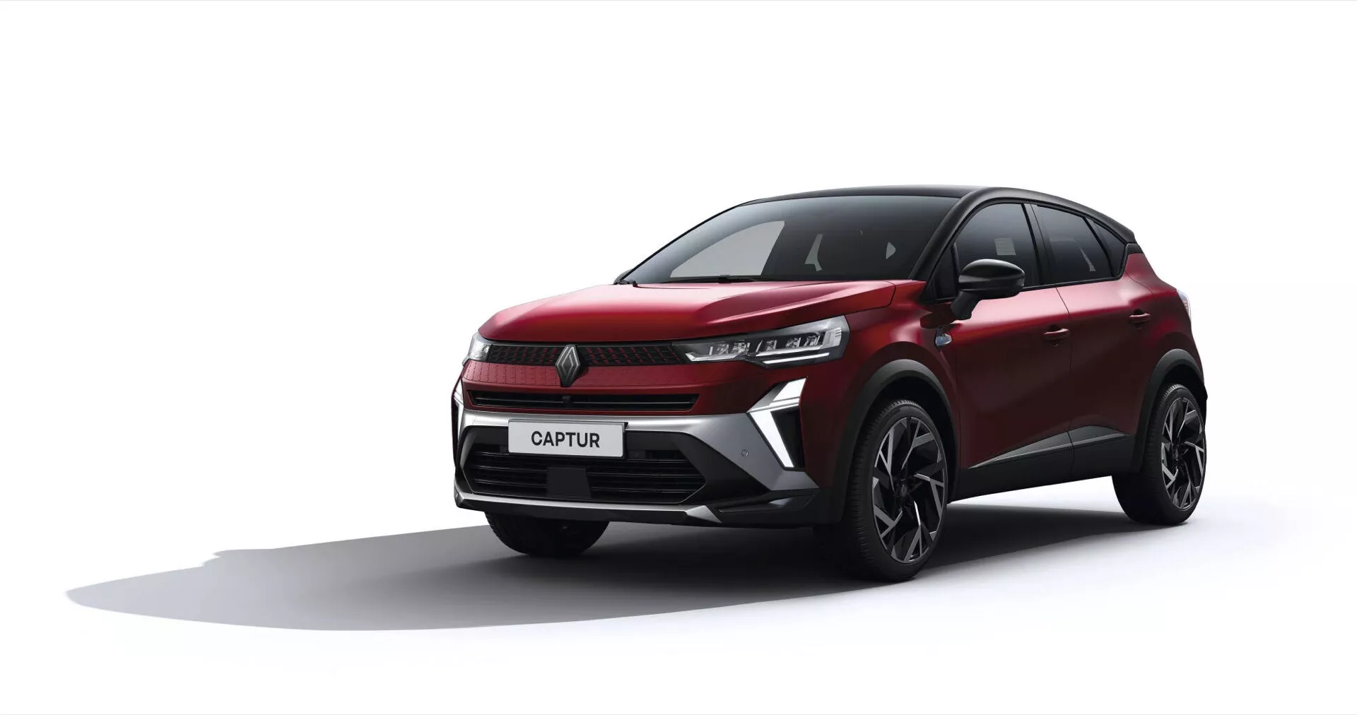 Facelift model Renault Captur 2024 v nízkoúhlém pohledu zepředu a ze strany zobrazující LED světlomety, dynamické linie karoserie a slitinová kola s vícepaprskovým designem na jednoduchém šedém pozadí