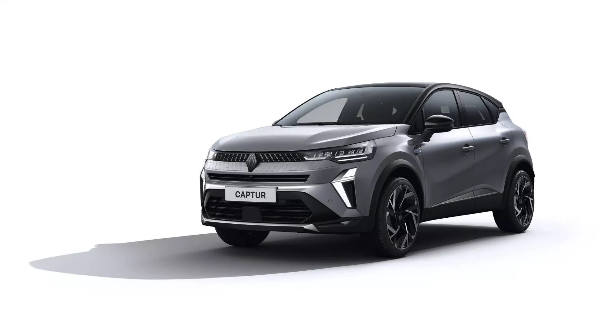 Renault Captur 2024 (II-Facelift) představen v studiovém prostředí, zobrazuje tříčtvrteční přední pohled, který zdůrazňuje přední mřížku, elegantní LED světlomety, tvarovanou kapotu a stylová slitinová kola na pozadí postupně přecházejícím od bílé k světle šedé