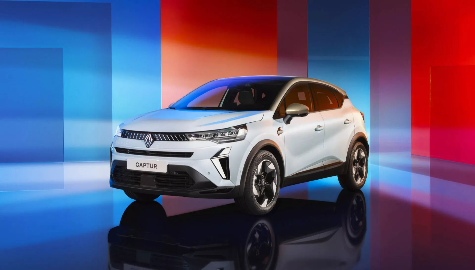 Facelift Renault Captur 2024 zobrazující tříčtvrteční přední pohled bílého kompaktního SUV na digitálně vytvořeném pozadí s červenomodrým přechodem, zdůrazňující moderní LED světlomety, výraznou masku s logem výrobce, dynamické linie, sochařské linie kapoty, elegantní linii střechy a velká vícepaprsková kola z lehkých slitin.
