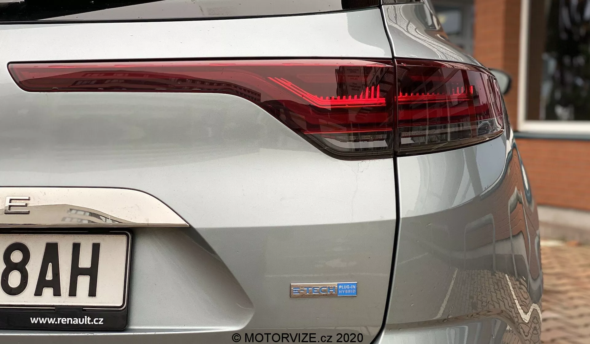 Pohled na zadní roh kovově stříbrného Renaultu Megane 2022 E-TECH, zobrazující pravé zadní světlo s moderními LED prvky a odznak E-TECH na zadním kufru. Viditelný je také zadní nárazník a částečný oblouk kola, což naznačuje, že auto je hybridní nebo elektrické.