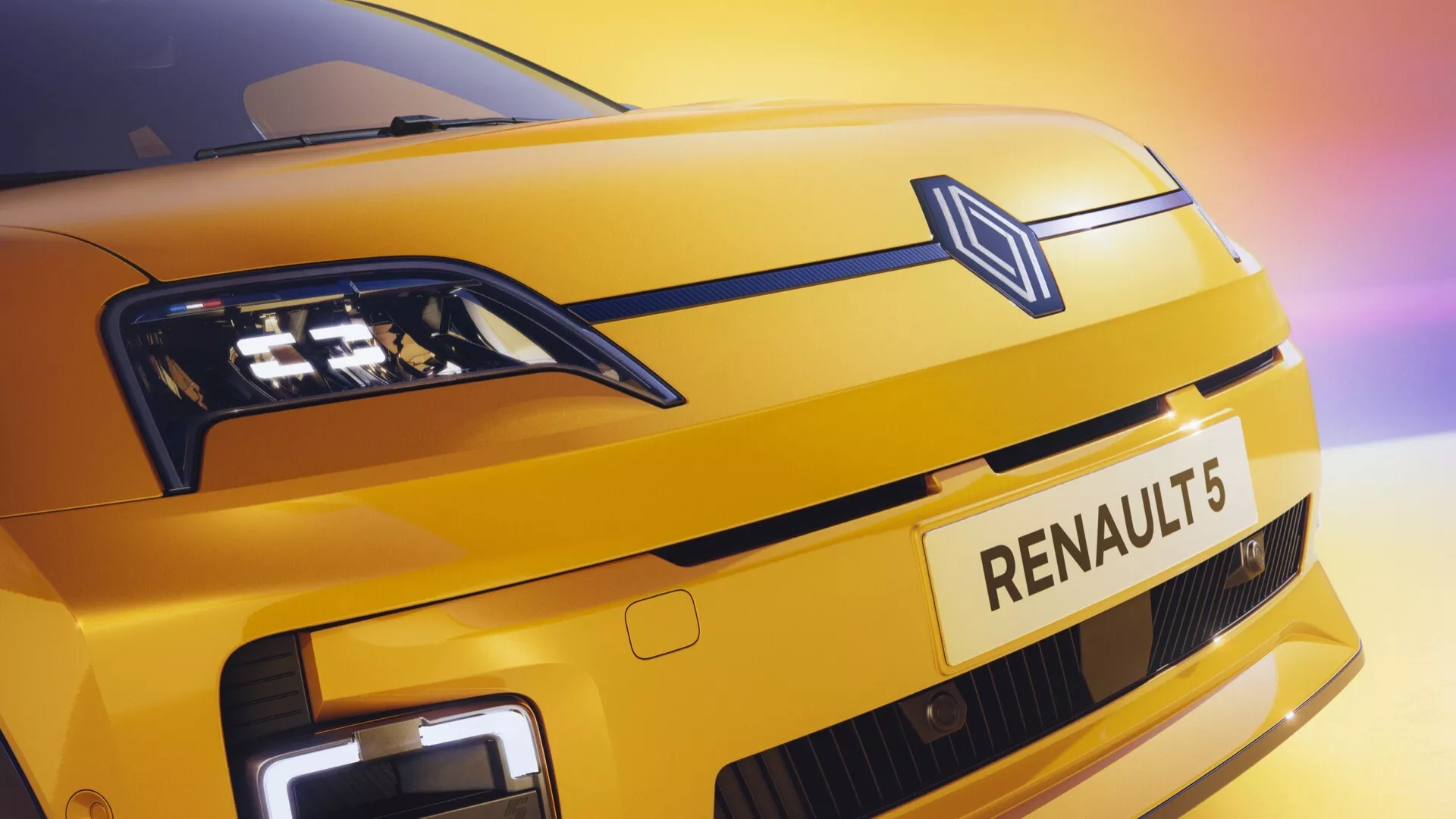 Detailní pohled na přední část Renaultu R5 2024 s metalickým žlutým lakem, diamantovým logem, LED světlomety a denními svíceními s moderně uzavřenou mřížkou naznačující elektrickou technologii pod silným výhledem zdůrazňující prvky značky a designu