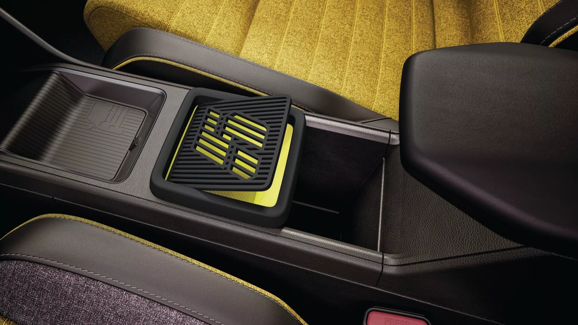 Detail interiéru Renault R5 2024 s detailním zobrazením oblasti centrální konzole, včetně otevřeného úložného prostoru s texturovanou podložkou, sousedícího moderního ventilačního systému s geometrickým designem a žlutozelenými akcenty na černém pozadí, kontrastních textur a jasného žlutého sedadla zadního sedadla s červenou sponou pásu naznačující důraz na bezpečnost pasažérů.