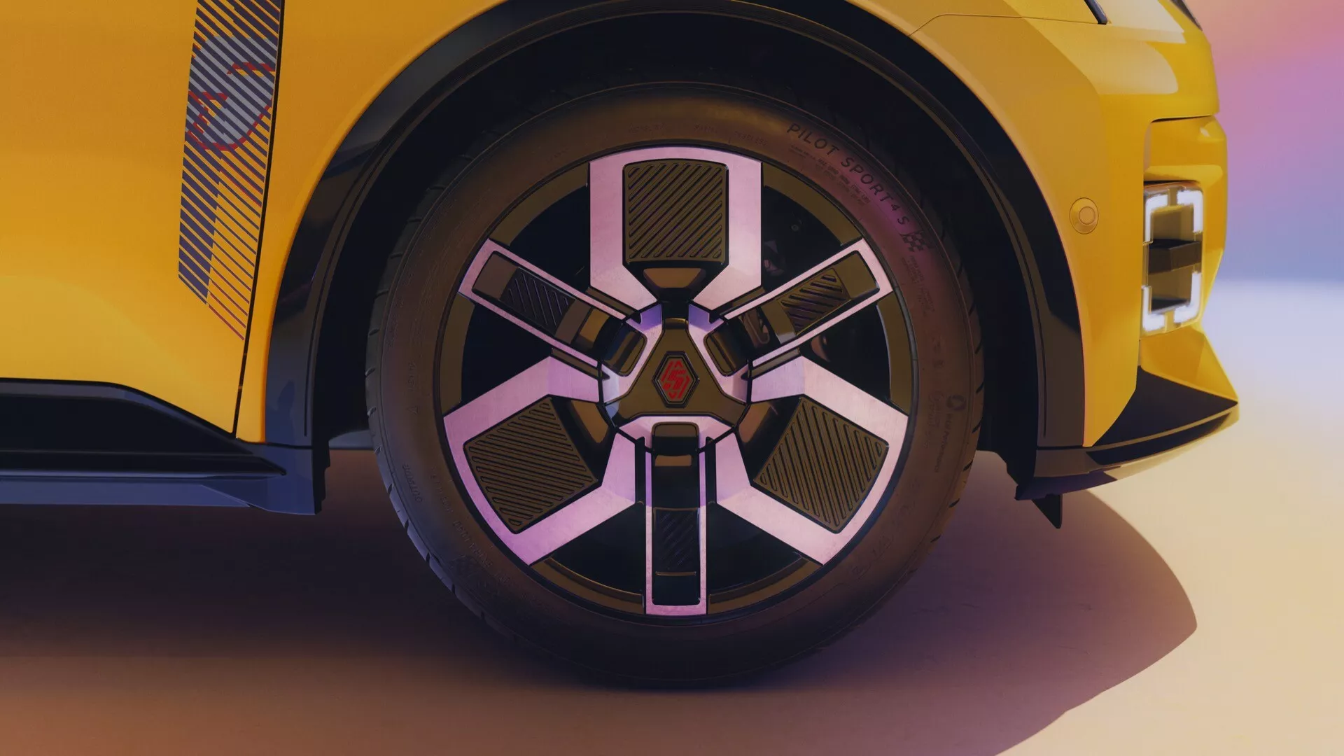 Detailní pohled na přední kolo Renault R5 2024 s moderním, geometrickým designem více paprsků v barvách stříbrné a černé, což naznačuje sportovní a prémiový estetický vzhled proti živě žluté karoserii, což naznačuje vysoký výkon a luxus.