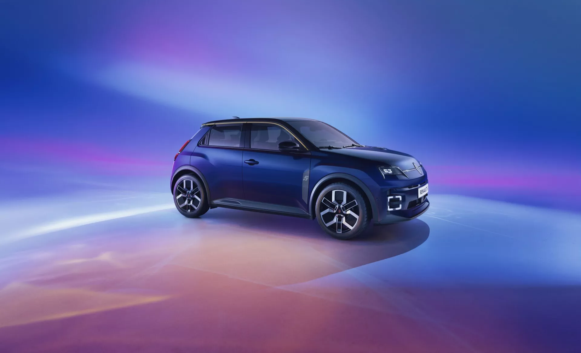 Kompaktní SUV Renault R5 2024 v metalické modré barvě prezentuje čelní a boční pohled ve tříčtvrtečním úhlu se světlomety LED, mřížkou chladiče zdůrazněnou chromem s logem, aerodynamickými liniemi na kapotě, bočním profilem s litými koly o více paprscích, obroučkami oken z leštěného kovu a tmavě tónovanými okny na digitálně přidaném přechodovém pozadí přecházejícím od fialové přes modrou do teplých tónů oranžové a červené