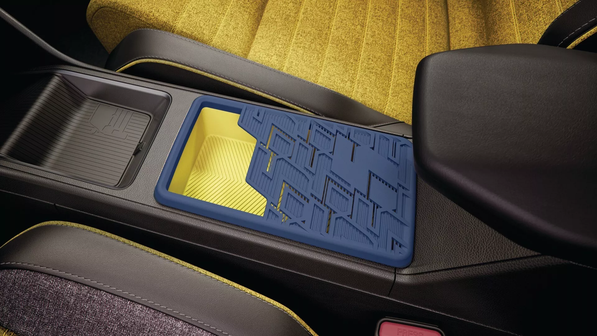 Detailní pohled na interiér Renault R5 2024 s centrální konzolí s modrým geometrickým vzorem úložného koše, černou konstrukcí, sousedícím držákem nápojů s gumovou vložkou a částečným pohledem na sedačky potažené látkou v žluté a černé barvě