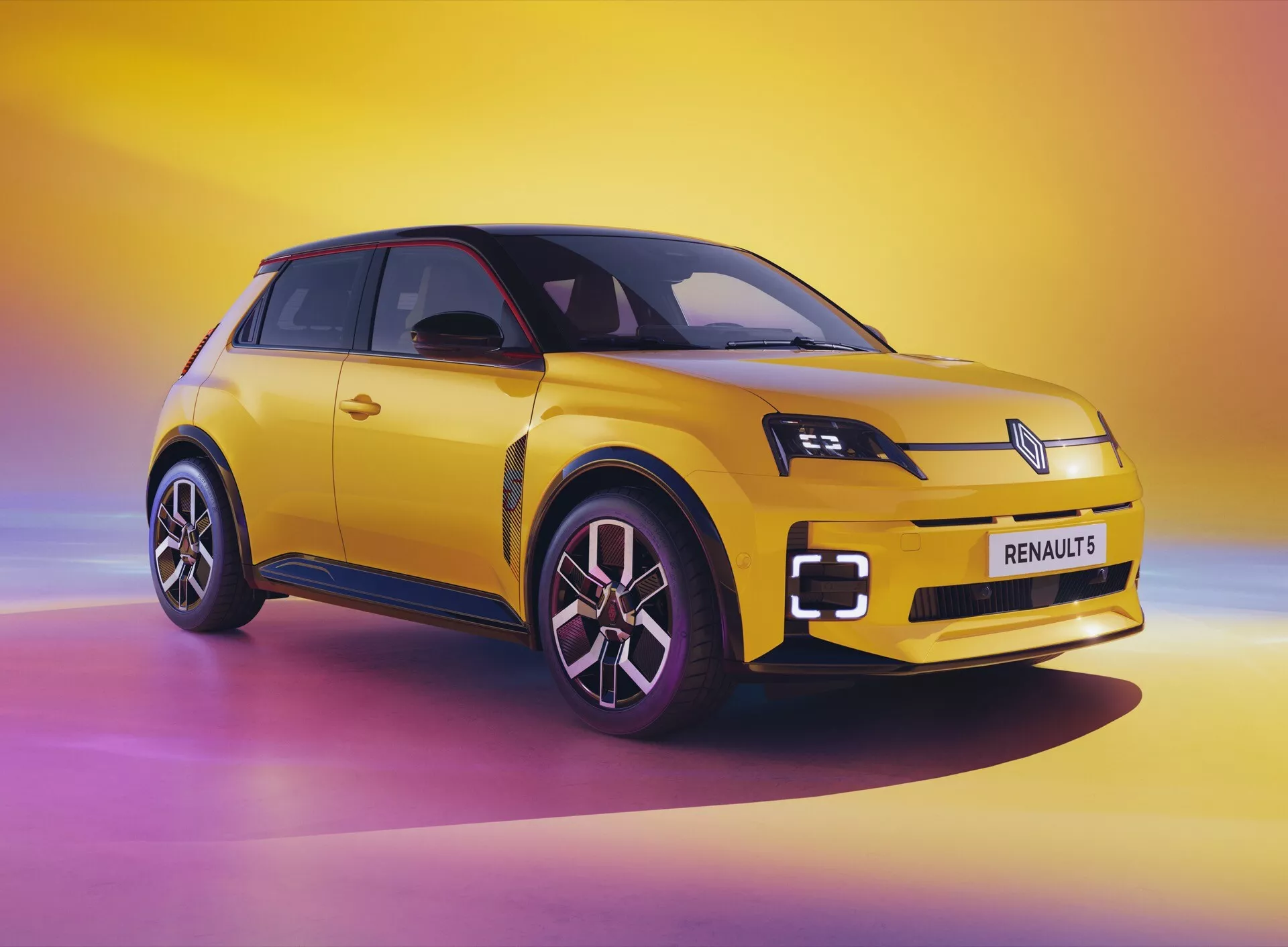 Renault R5 2024 ve studiu s dynamickým pozadím přecházejícím od růžové přes žlutou po fialovou, předvádějící moderní design, LED světlomety, aerodynamické slitinové kola a nápadnou žlutou barvu v mladistvém a stylovém provedení.