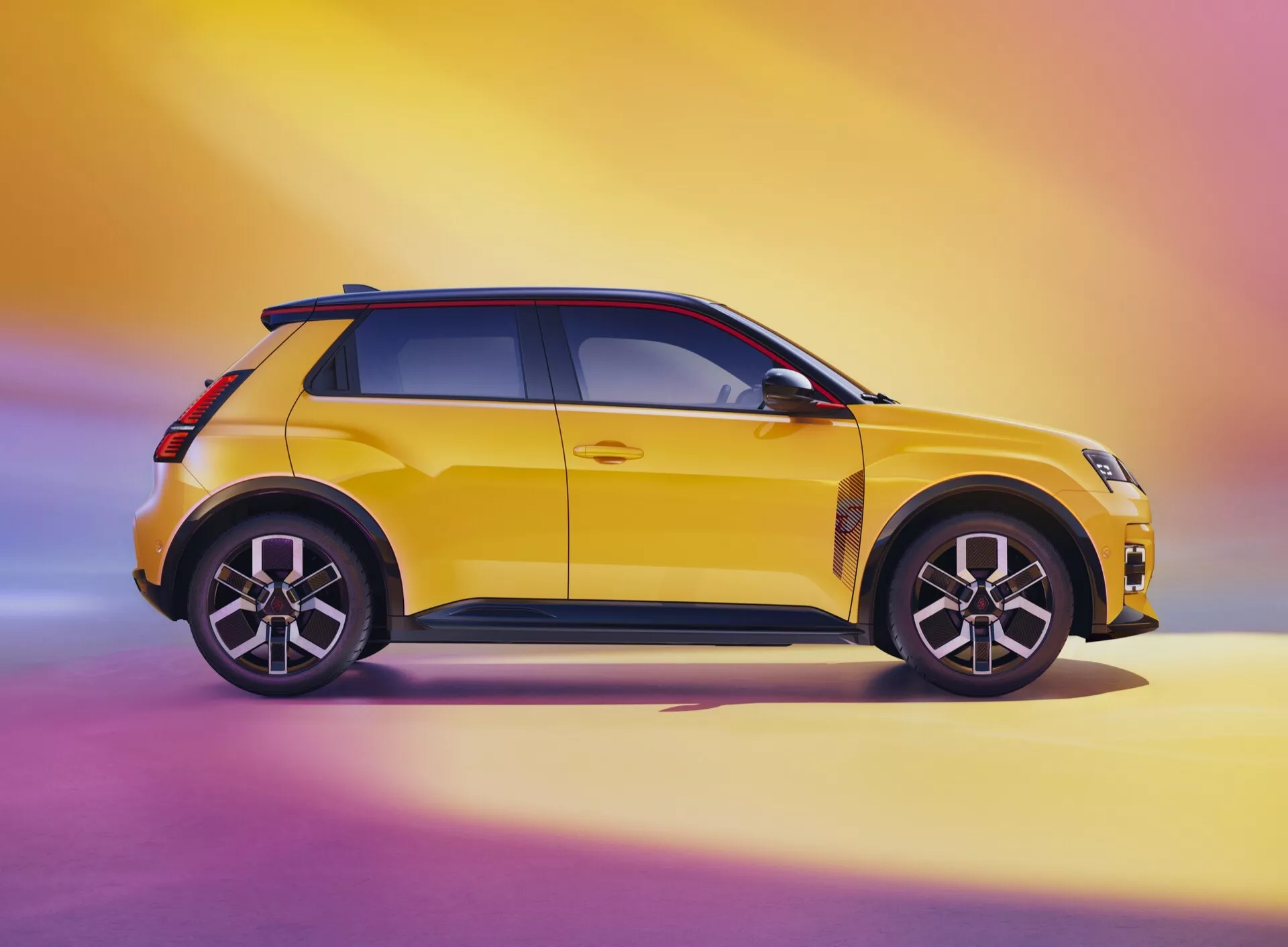 Boční profil Renaultu R5 2024 ve výrazné žluté s kontrastní černou střechou a kryty zrcátek na pozadí přechodu z růžové do žluté, zdůrazňující moderní designové prvky, LED osvětlení a aerodynamické kontury