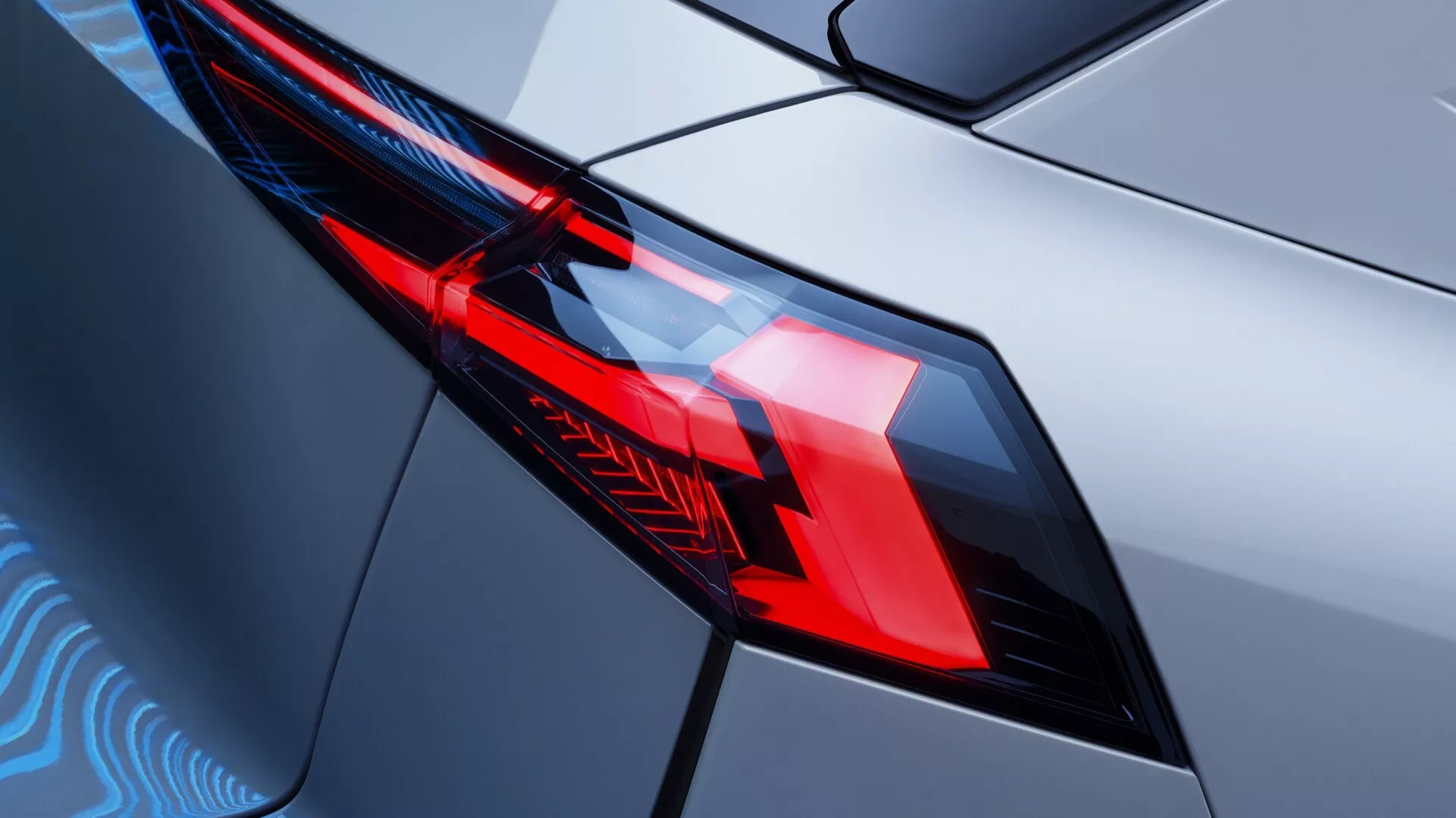 Detailní záběr na zadní světelnou soustavu Renault Symbioz 2024 generace, ukazující propracovaný design a moderní LED osvětlení. Diagonální pohled ze zadního rohu se zaměřuje na levé zadní světlo z lehce zvýšeného úhlu, zvýrazňující geometrické tvary, ostré světelné vzory a oddělené části pro brzdová a zpětná světla. Kryt světla s ostrými hranami těsně zapadá do karoserie vozu s lesklým kovovým povrchem, který odráží moderní design a technologické prvky vozidla.