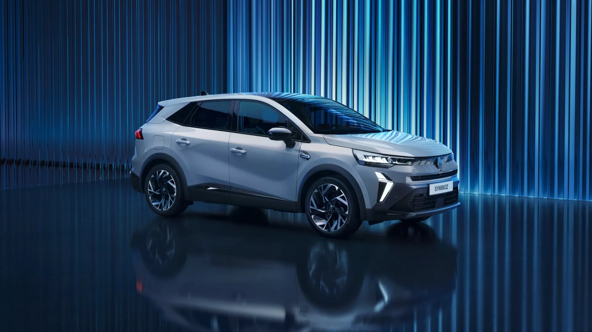 Digitální studio zobrazení 2024 Renault Symbioz 1. generace, moderní SUV s elegantním, dynamickým designem. Profilový pohled z mírného předního úhlu, který zobrazuje boční profil, přední část, mřížku, světlomety, kola a boční zrcátka. Středová polohovka v rámečku, fotografie z nízkého úhlu zdůrazňující silný postoj vozu. Ostrá, úhlová světlomety naznačující LED technologii a denní světla. Úzká vodorovná mřížka zdůrazňující aerodynamiku. Sochařská charakterová linie od přední části k zadní části pro aerodynamický vzhled. Kola s vícepaprskovým designem ze slitin zvyšují sportovní vzhled. Reflexní povrch pod vozidlem a modré abstraktní digitální pozadí vytvářejí prémiovou, futuristickou estetiku, která možná naznačuje moderní nebo dokonce elektrickou pohonnou technologii.