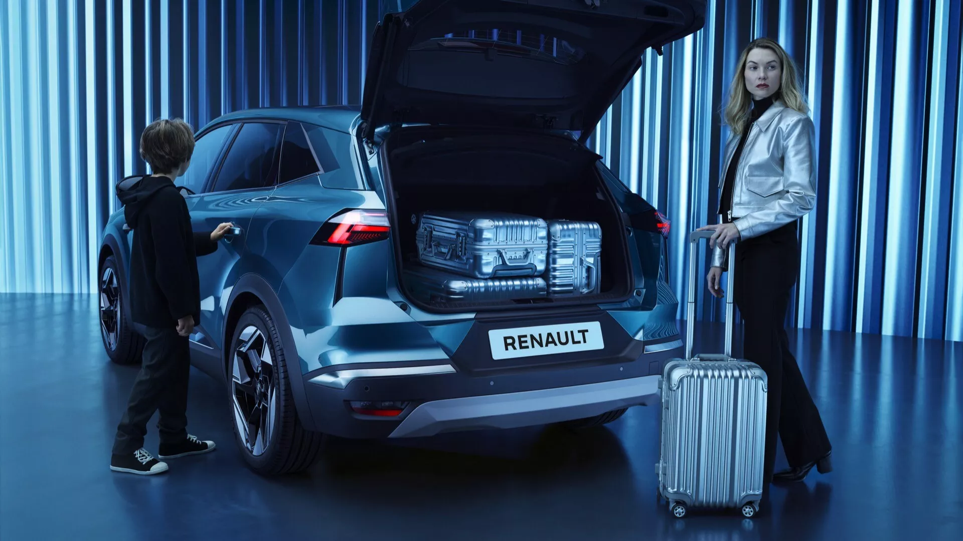 Renault Symbioz 2024 SUV v kovové barvě v úhlu 45 stupňů, zobrazující zadní a částečný boční profil se sochařským moderním designem. Otevřený zadní kufr, odhalující prostor pro zavazadla a naznačující užitné prvky jako automatický zdvihací otvor. Výrazné LED zadní světla a prominentní logo Renault na kufru. Vystavený ve dobře osvětleném studiu s modrým pozadím. Žena stojí u zadní části na straně spolujezdce držící zavazadlo, dítě sahá k otevřenému kufru, což značí rodinně přívětivý design. Viditelná varovná kola. Zaměřeno na design vozu a vlastnosti v nejednoznačném prostoru.