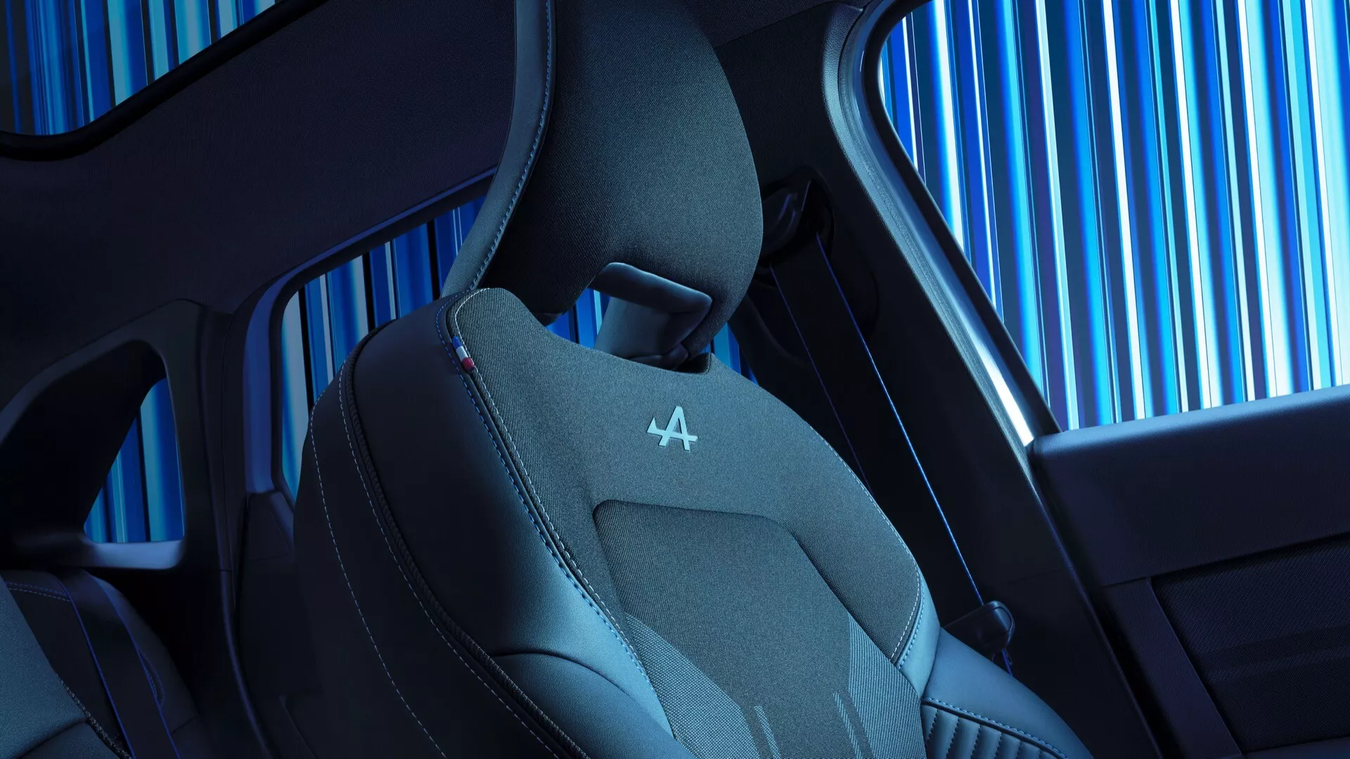 Zblízka pohled na interiér sedadla 2024 Renault Symbioz první generace, zdůrazňující moderní design a technologické funkce. Ukázka horní části sedadla s ergonomickým tvarem, tvarovanými bočními výztuhami a směsí kůže a prodyšné látky pro luxus a pohodlí. Výrazné červené prošívání na opěrce hlavy s reliéfním logem, včetně pohledu na vzorek bočního okna vozu a elegantní design kabiny.