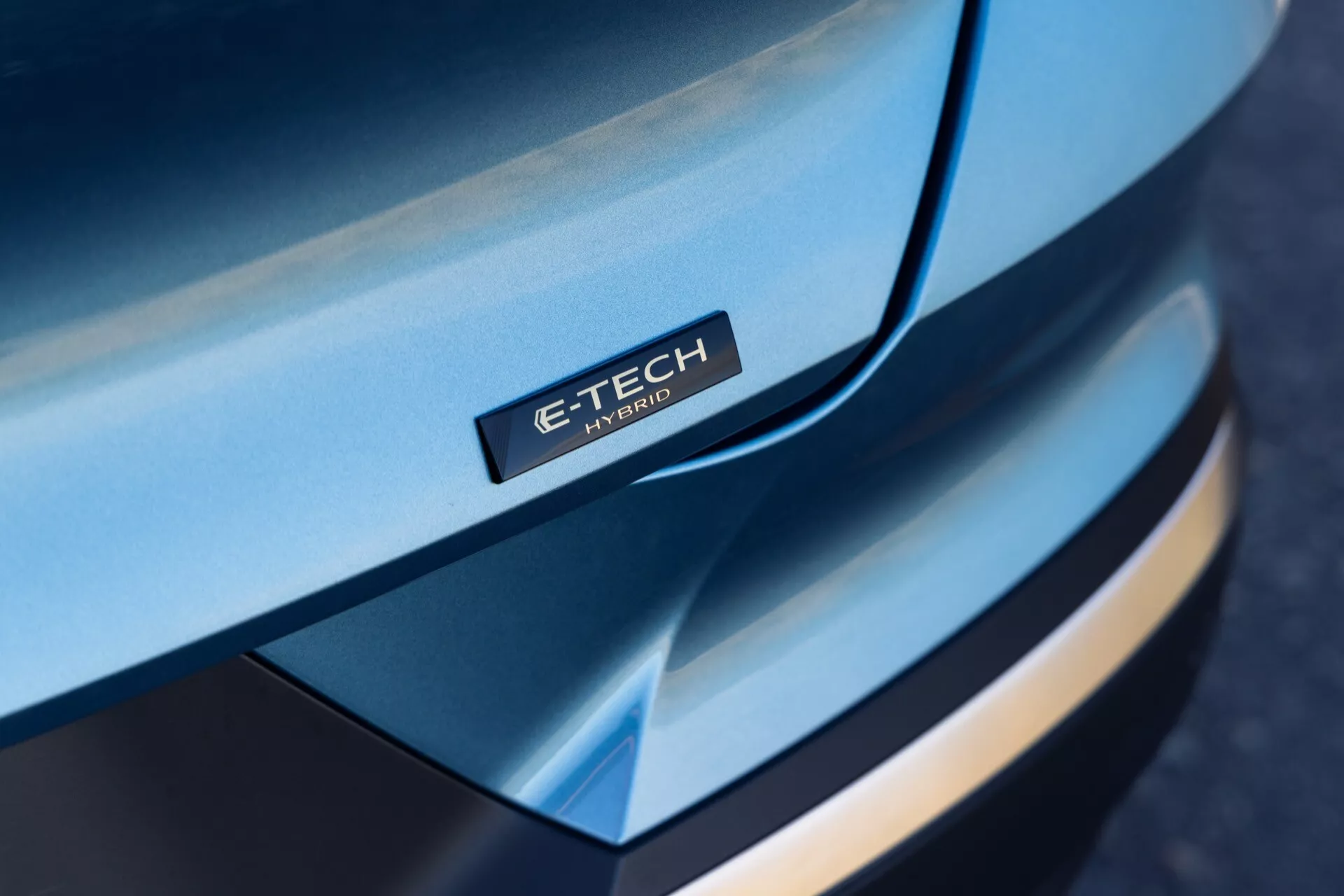 Detailní šikmý pohled na přední část Renaultu Symbioz 2024, zaměřující se na elegantní, zakřivenou kapotu s odznakem 'E-TECH Hybrid', vícevrstvým designem předního nárazníku, kontrastními barvami a prémiovým vzhledem, zdůrazňující hybridní technologii.