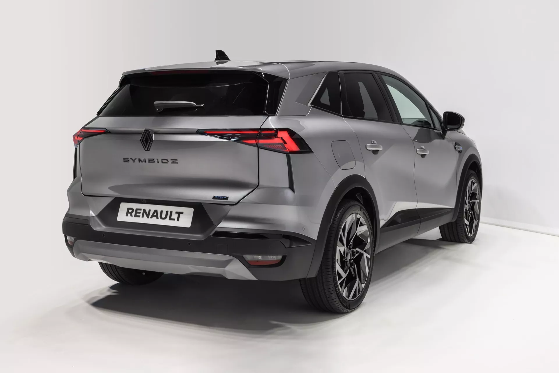 Obrázek ukazuje moderní SUV z trojčtvrťového pohledu zezadu, zvýrazňující tvarovaný zadní a boční profil. Mezi výrazné prvky patří horizontálně prodloužená LED zadní světla, skloněné zadní sklo s integrovaným spoilerem, senzory a kamera v zadním nárazníku pro bezpečnost a slitá kola s vícepaprskovým designem. Vozidlo je natřeno metalickou barvou, která zvýrazňuje jeho křivky a úhlový design. Na víku jsou prominentně umístěny branding a odznaky, které naznačují různé moderní vybavení jako bezklíčový vstup, zadní parkovací senzory a pokročilé osvětlovací systémy.