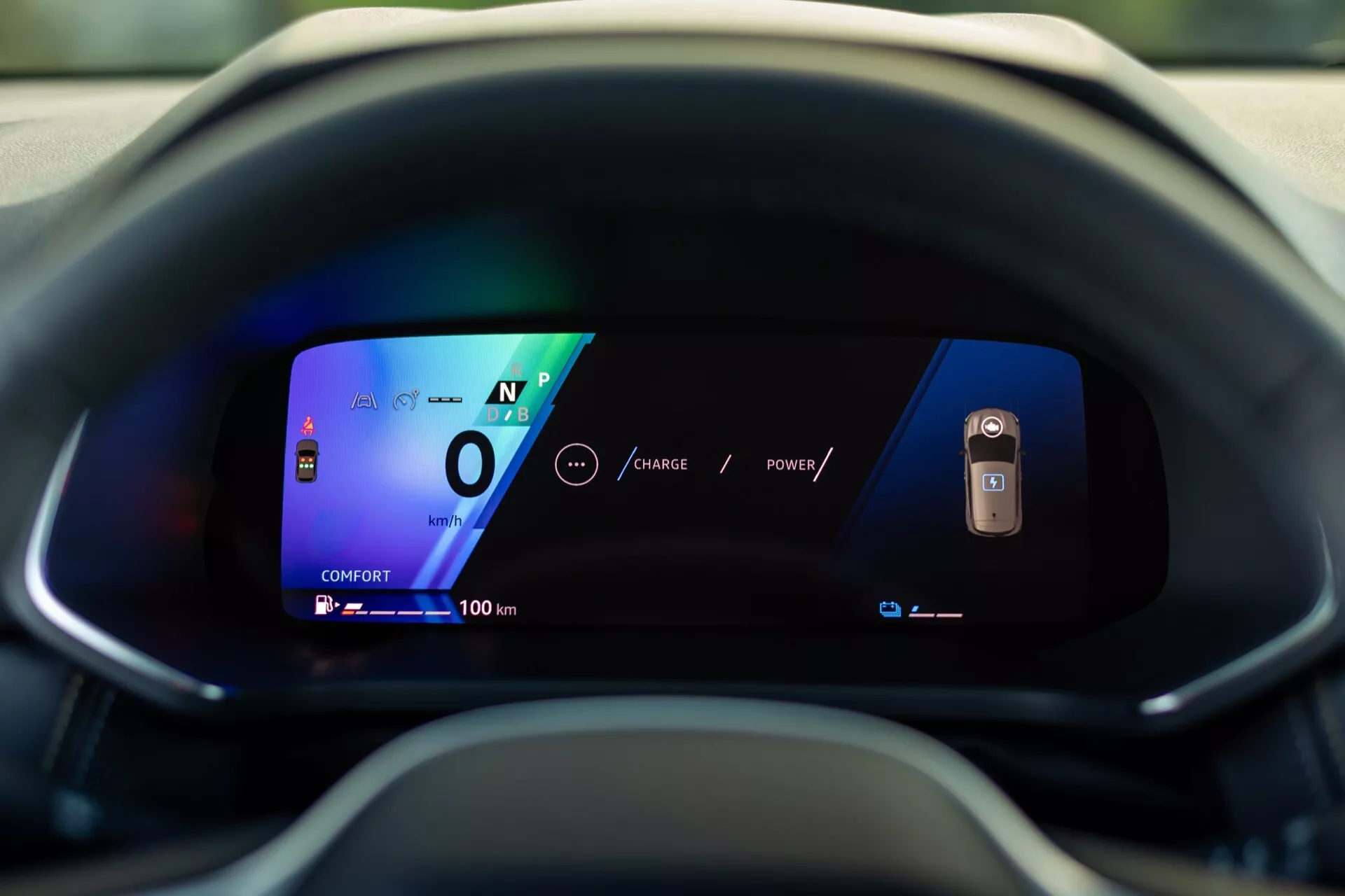 Detailní pohled na digitální přístrojovou desku modelu Renault Symbioz 2024 z perspektivy řidiče. Displej s živými barvami a jasnou grafikou na zakřivené obrazovce ukazuje vůz v neutrálu rychlostí 0 a dosah 100 km, což zdůrazňuje jeho pokročilou, pravděpodobně elektrickou technologii a moderní design uživatelského rozhraní.