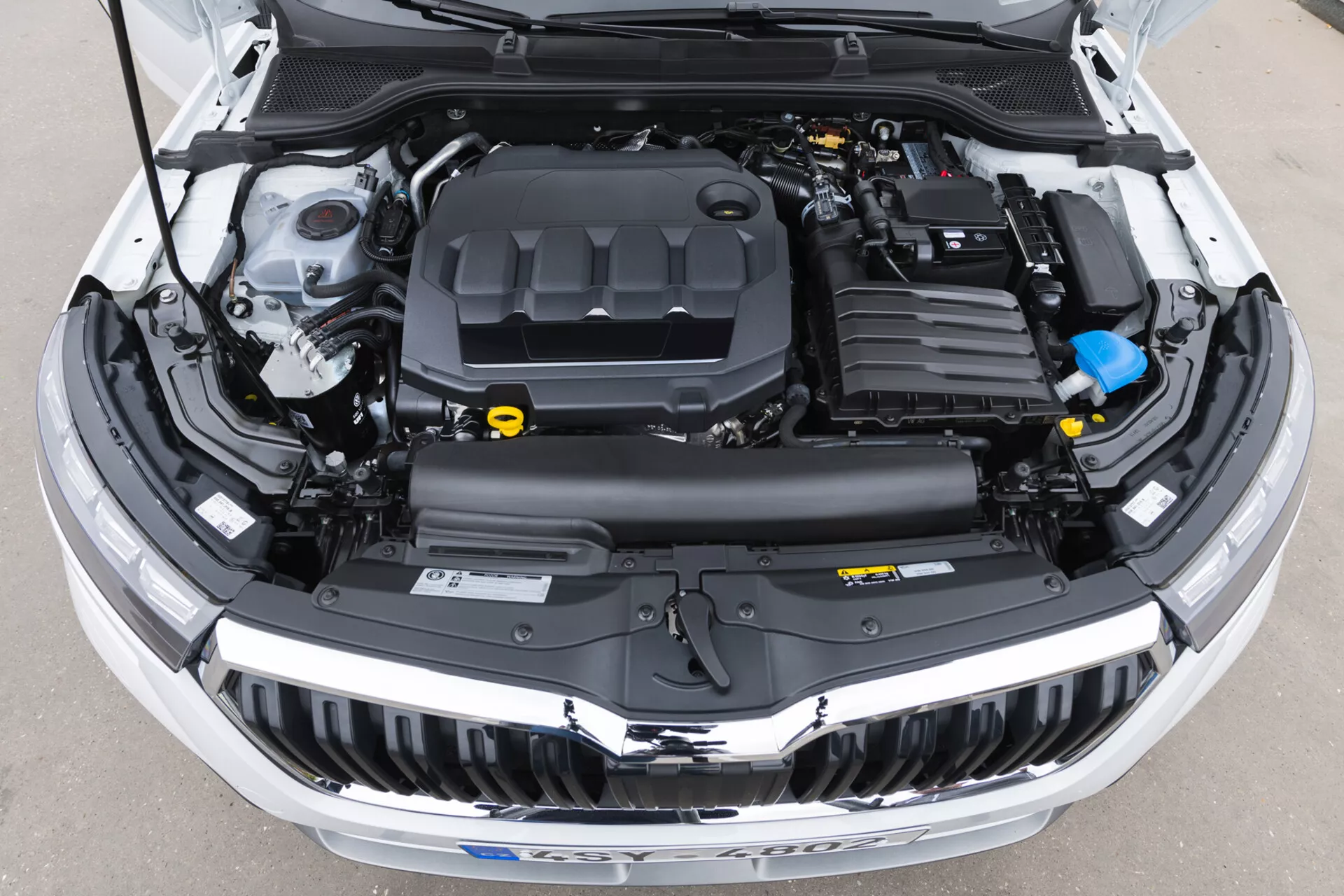 Detailní pohled na otevřený prostor motoru Škoda Kamiq 2019 s krytem motoru, plastovými kryty, nádržemi na kapaliny a elektrickými vedeními bez viditelných prvků vnějšího designu